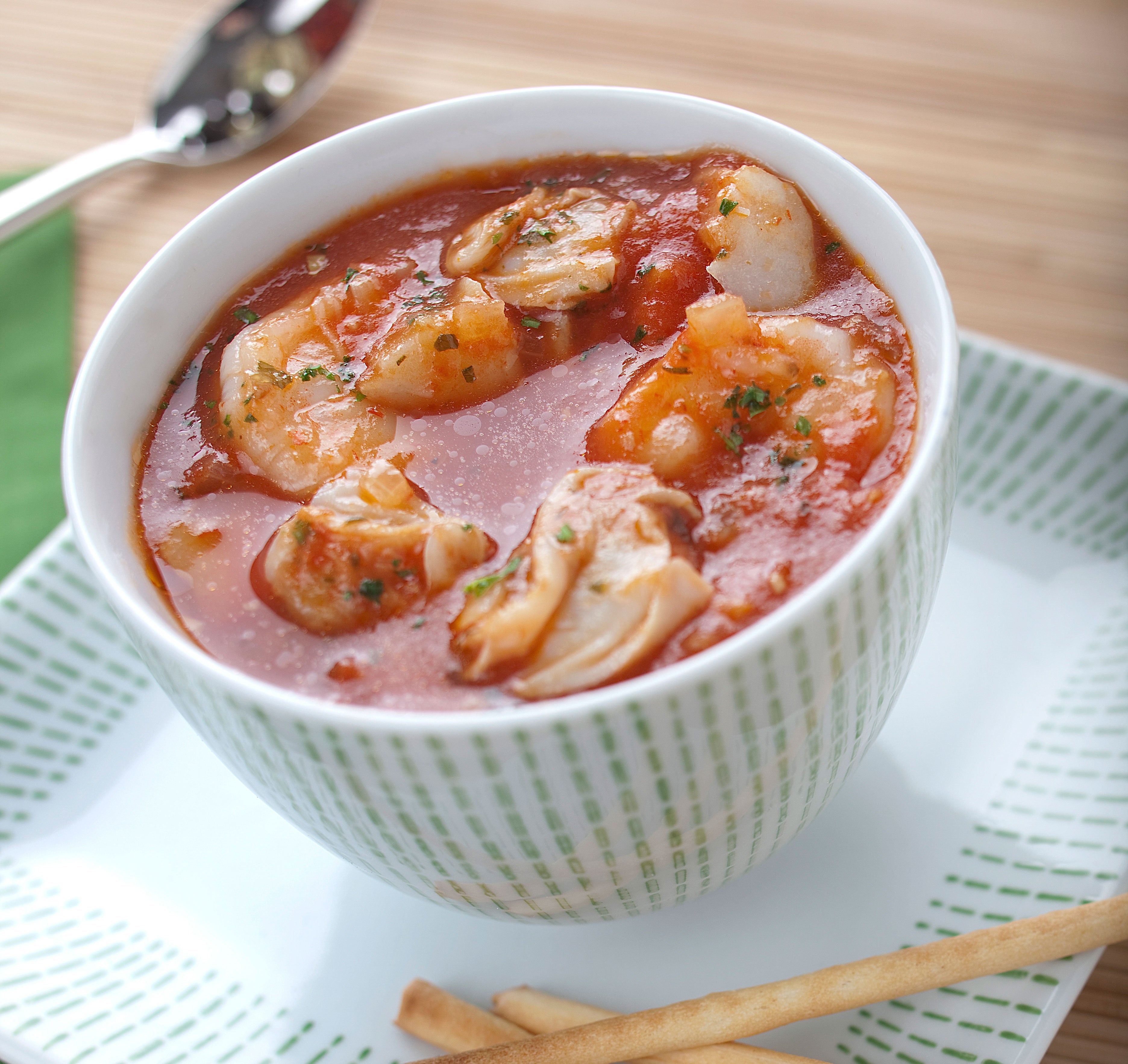 Bowl of seafood chowder with chunks of seafood and a garnish, served with breadsticks