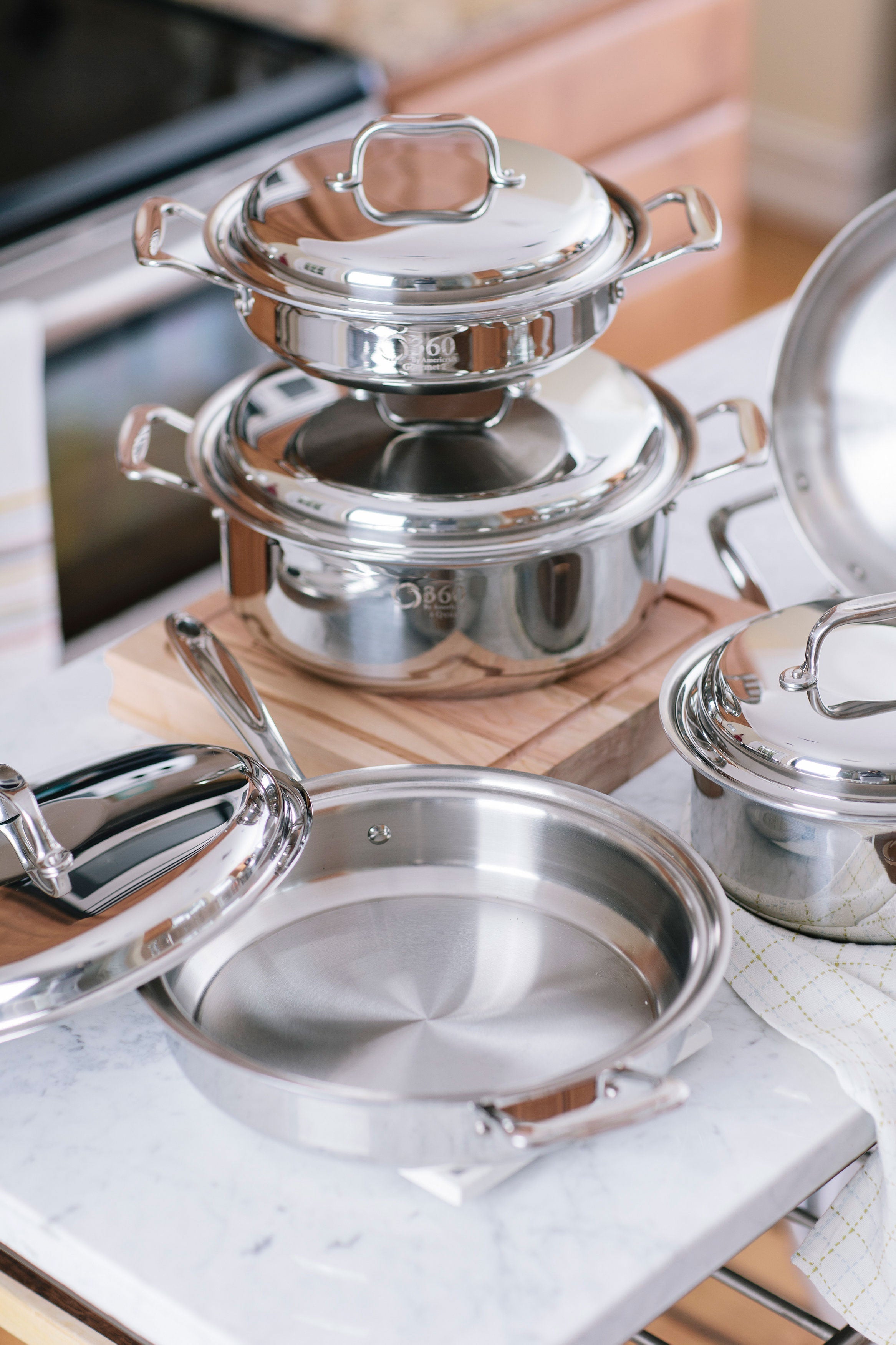 Angled view of stainless steel cookware set showing mirror finish, riveted handles and open skillet interior on a marble countertop