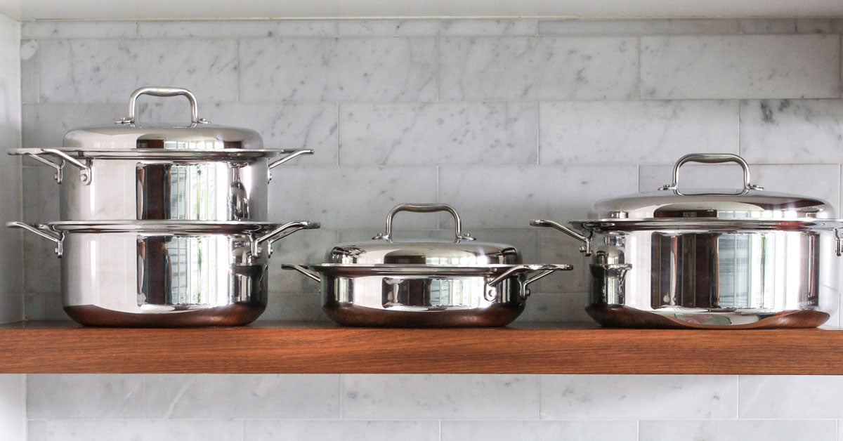 Three pieces of stainless steel 360cookware on a wooden shelf, showcasing their design and quality.