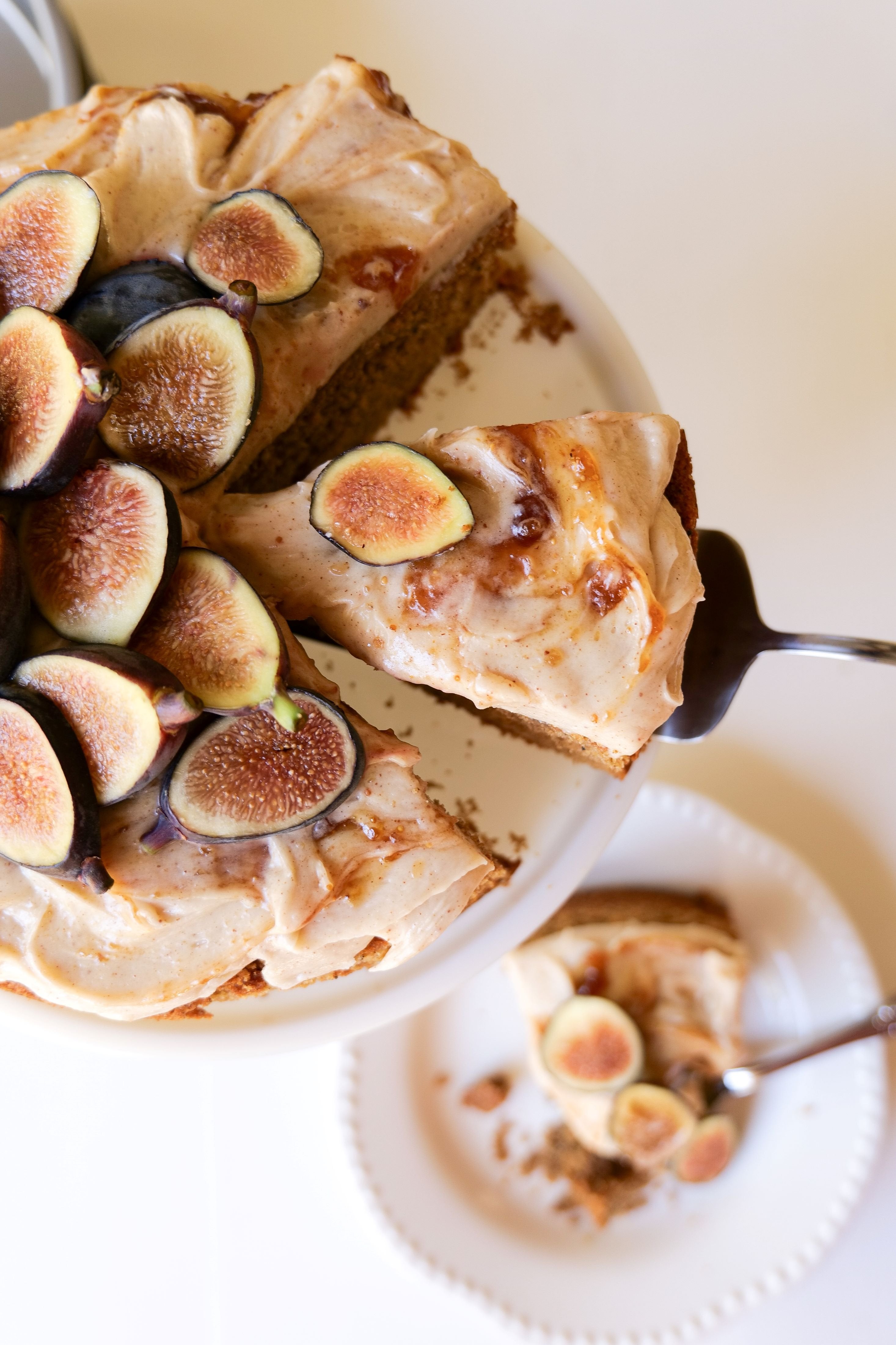 A slice of fig cake topped with fresh figs and cream cheese frosting on a white plate.