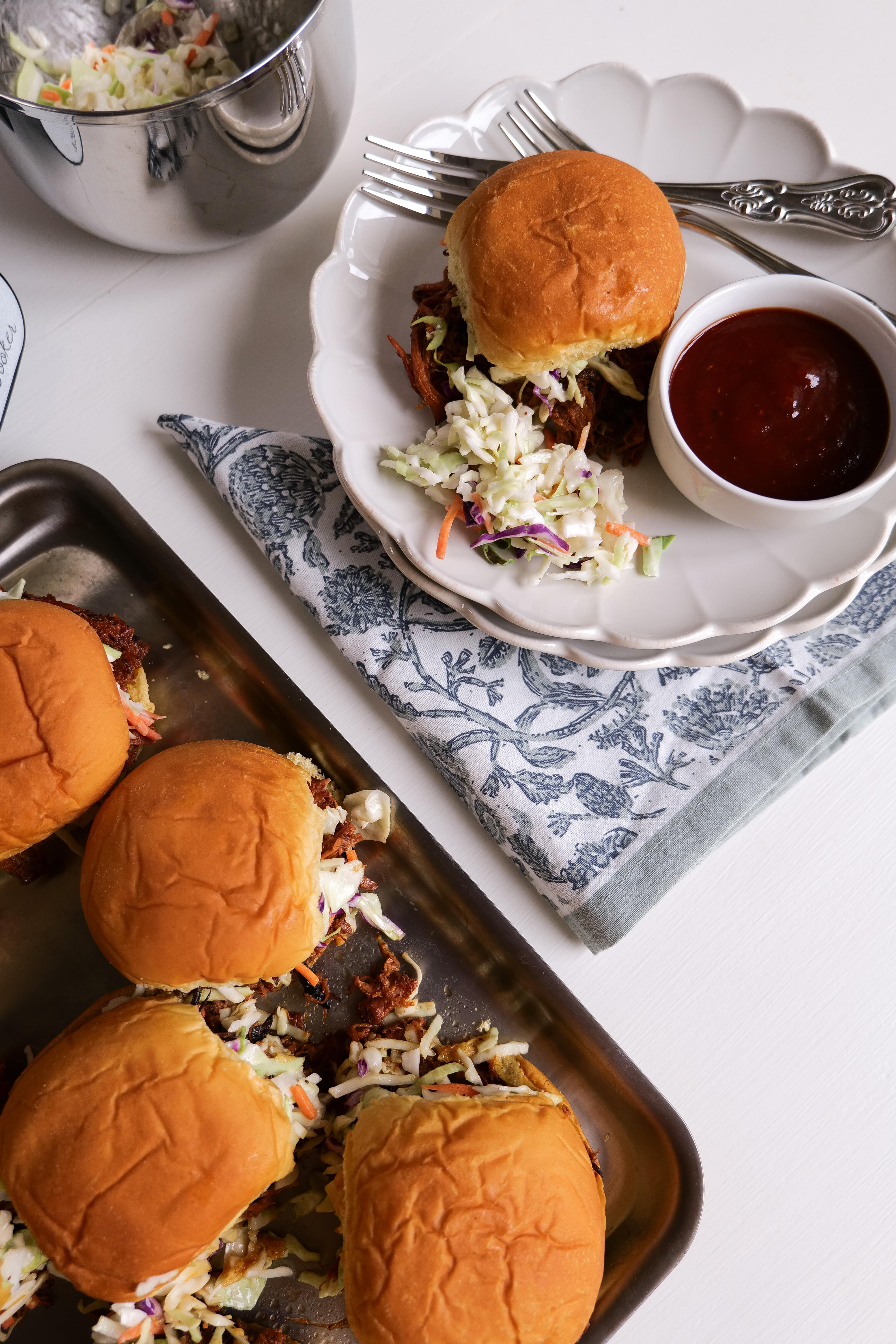 A tray of pulled pork sliders with coleslaw and barbecue sauce on the side