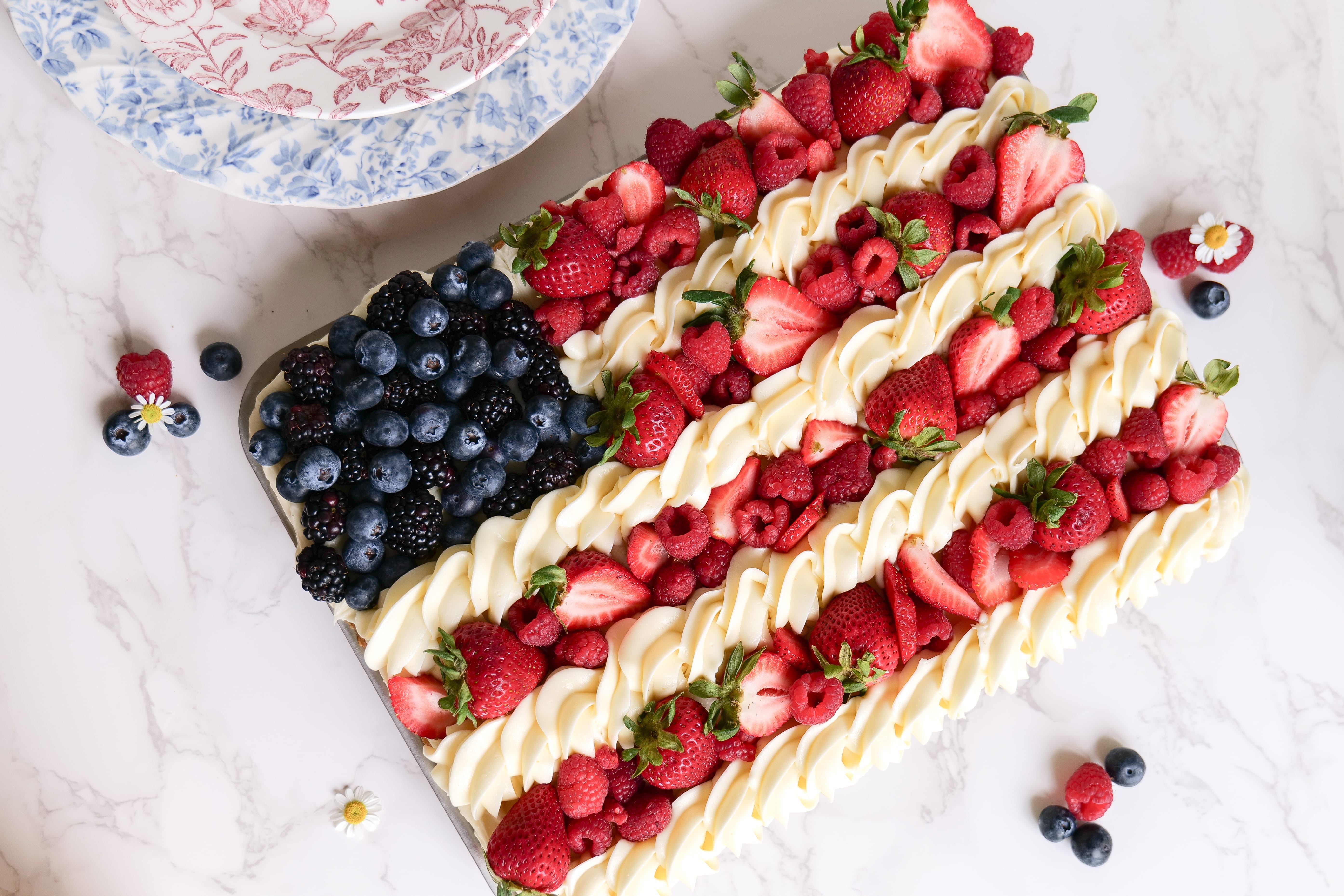 A fruit pizza decorated like an American flag with strawberries, blueberries, and whipped cream.