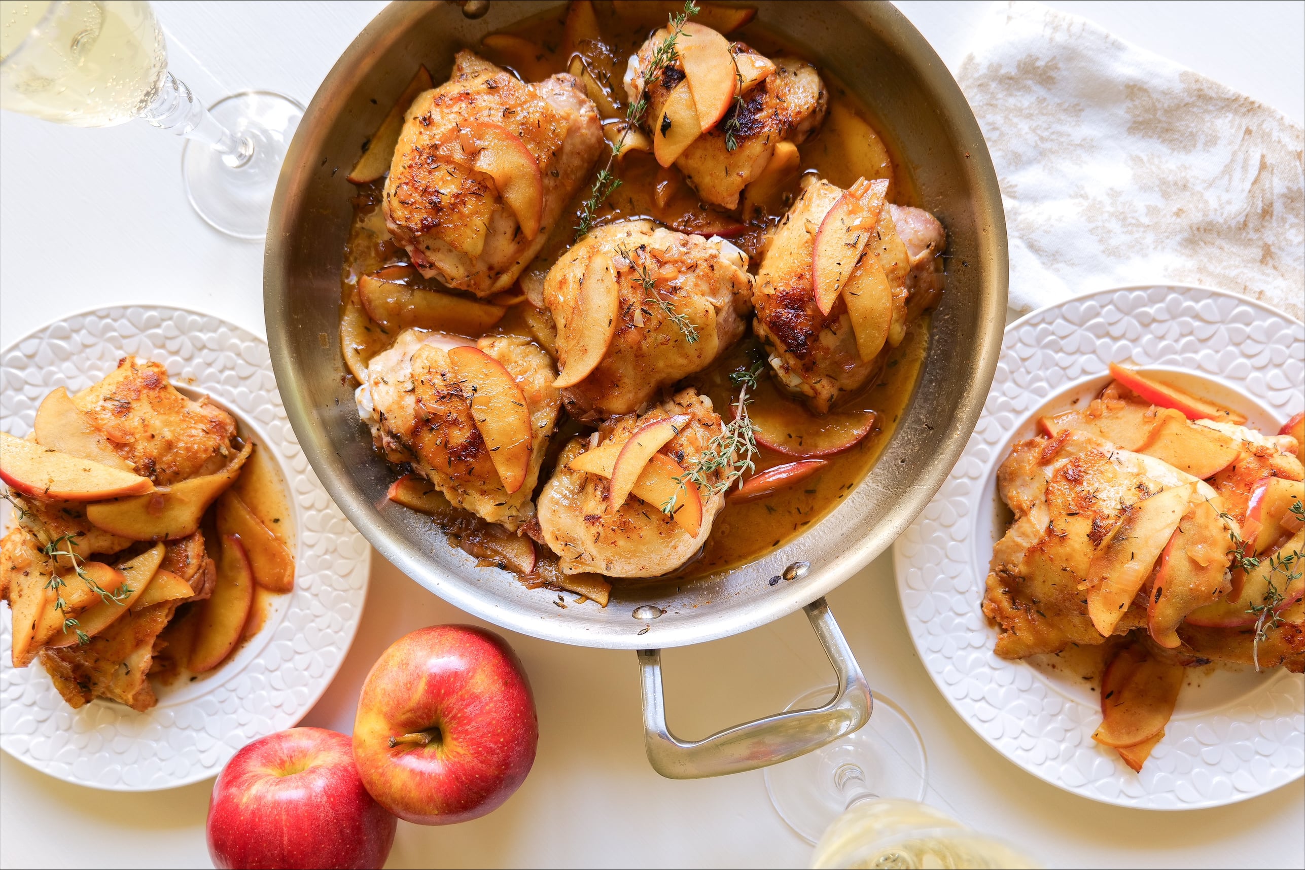 Apple glazed chicken thighs served with sliced apples and thyme, with red apples in the foreground