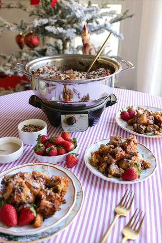 A serving of Slow Cooker Cinnamon Roll Casserole with strawberries on plates and a bowl of sauce on a table.