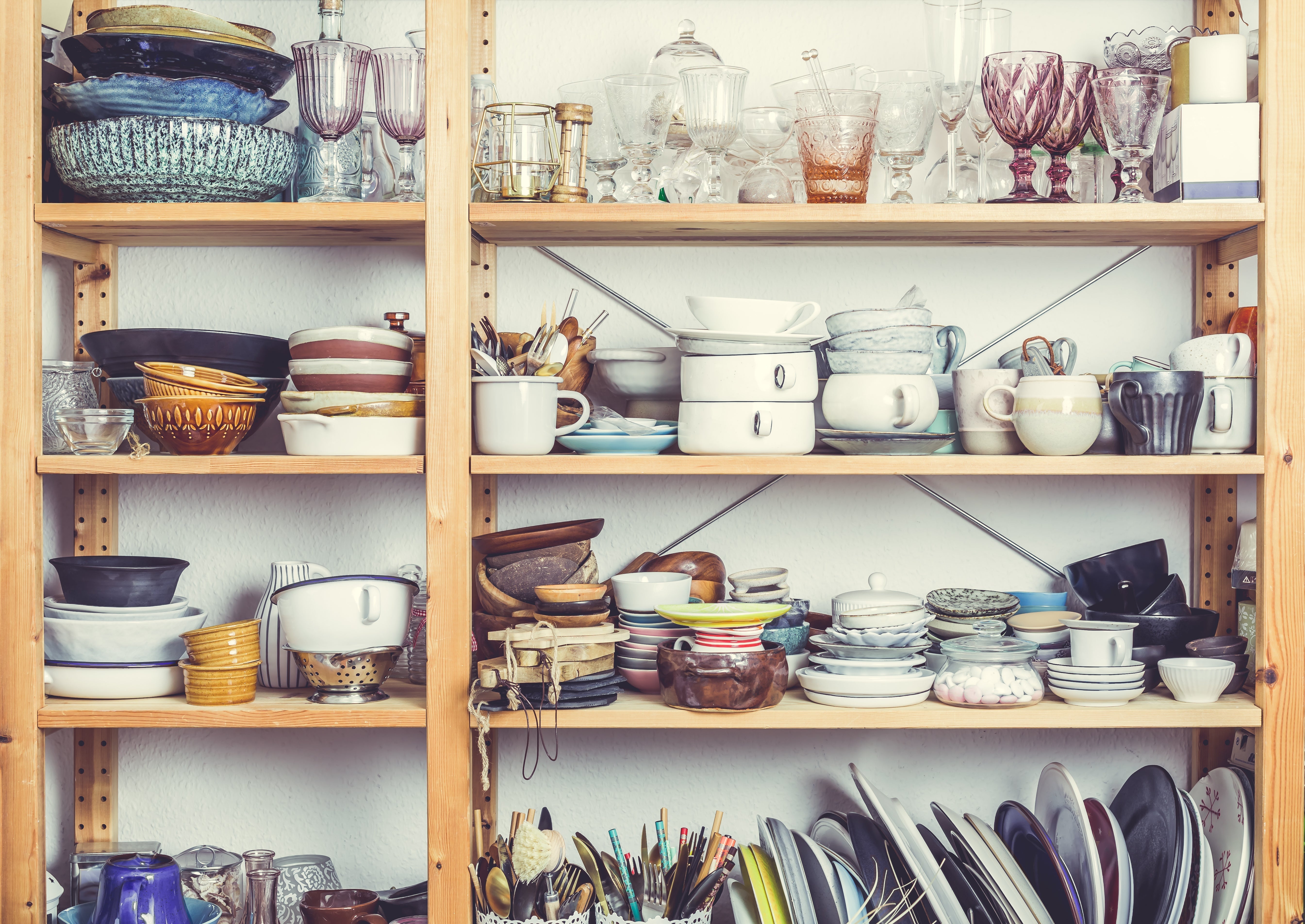 A cluttered kitchen shelf filled with various dishes, glasses, and utensils.