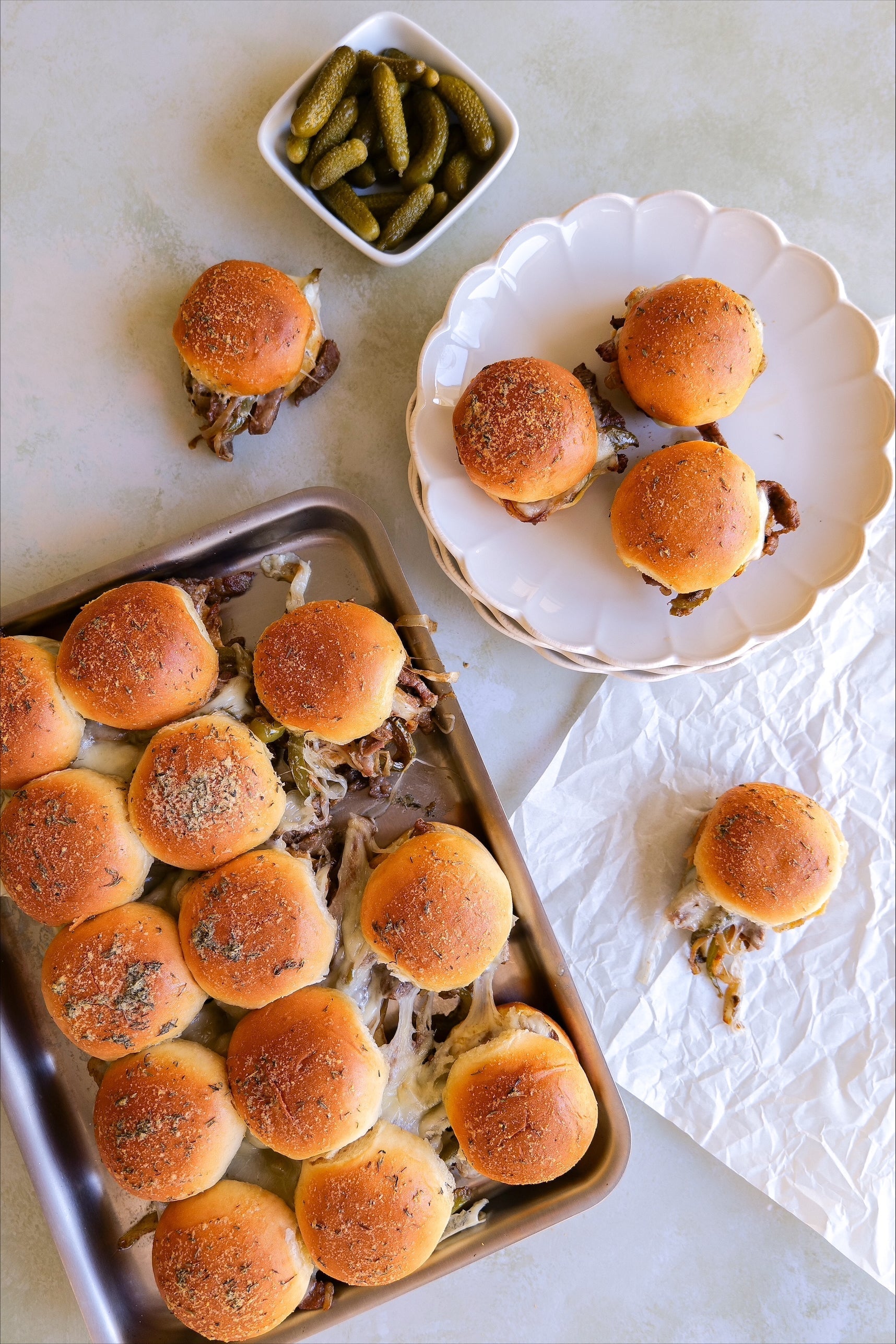 A tray of Philly cheesesteak sliders with pickles on the side