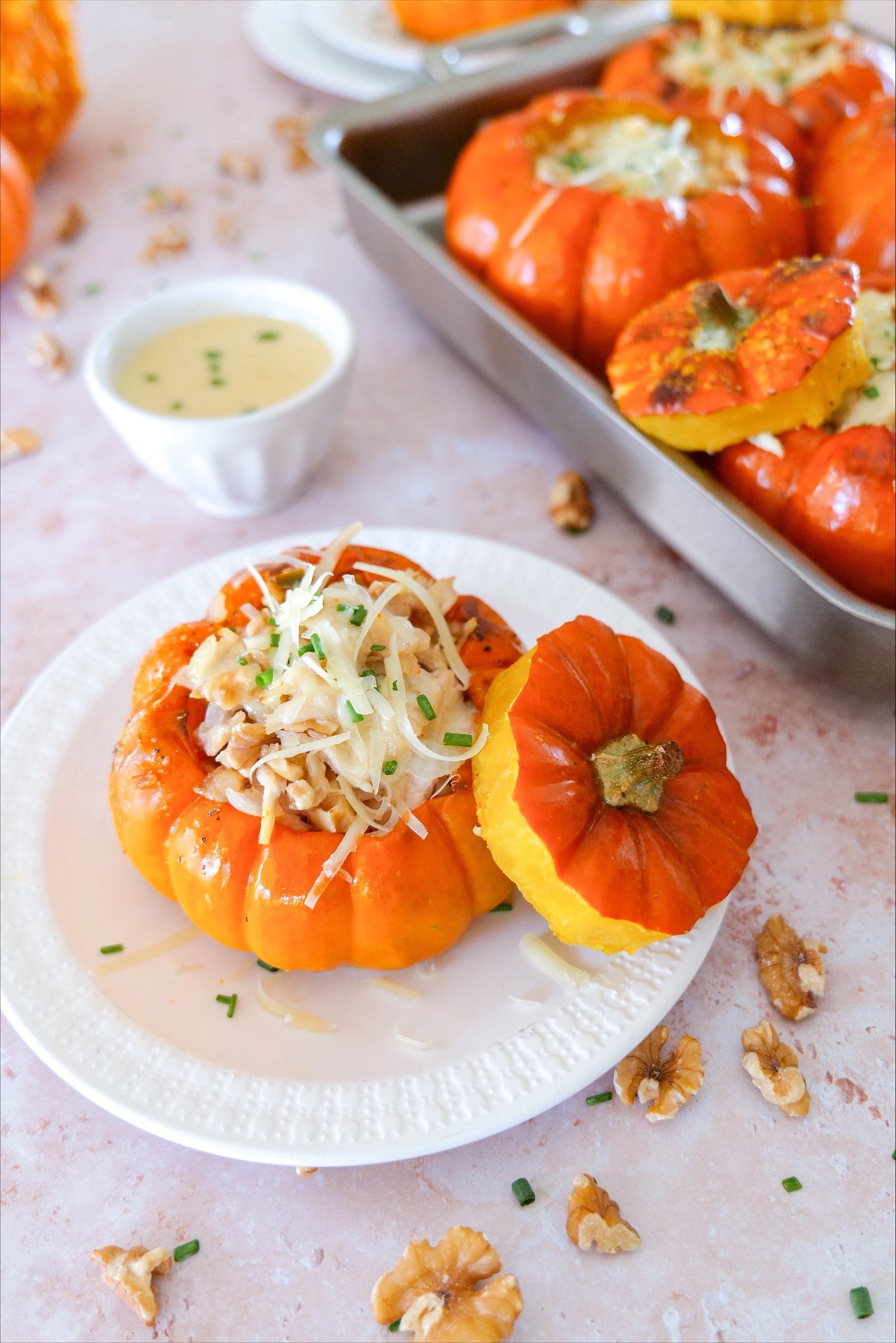 Roasted mini pumpkins stuffed with rice, cheese, and chives served on a white plate with scattered walnuts and a ramekin of sauce