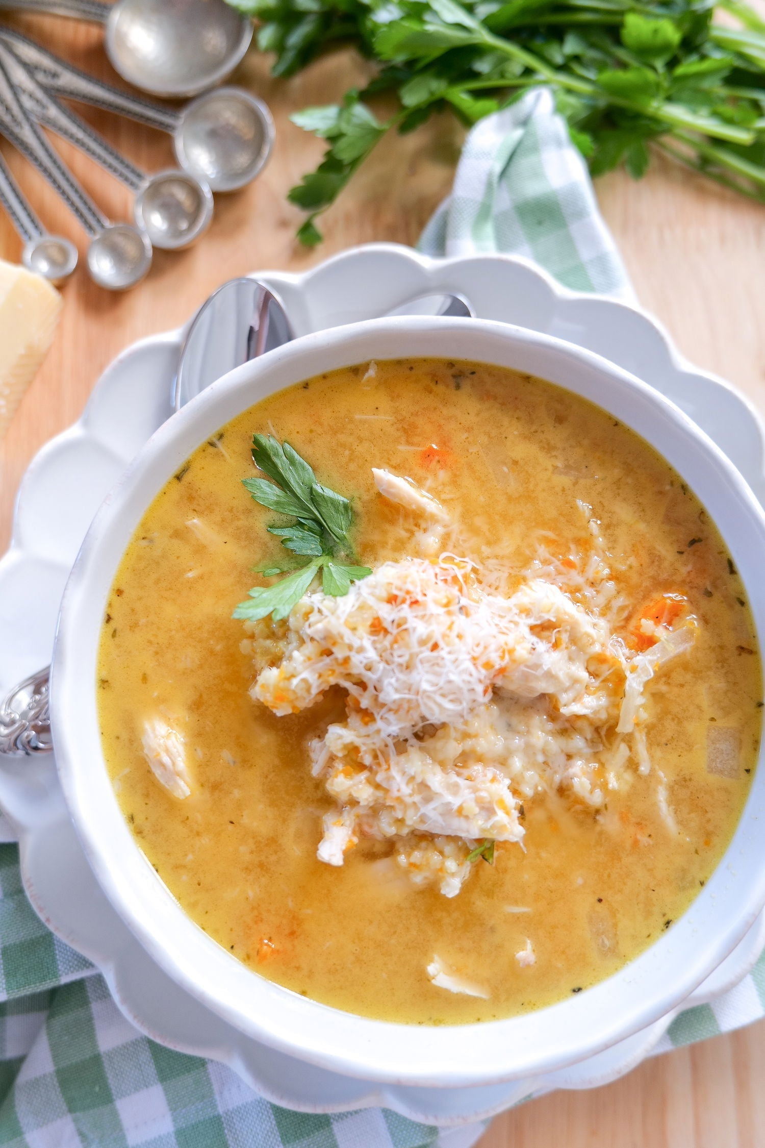 Overhead view of Italian Penicillin soup with shredded chicken, grated Parmesan and parsley in a white bowl on a wooden board