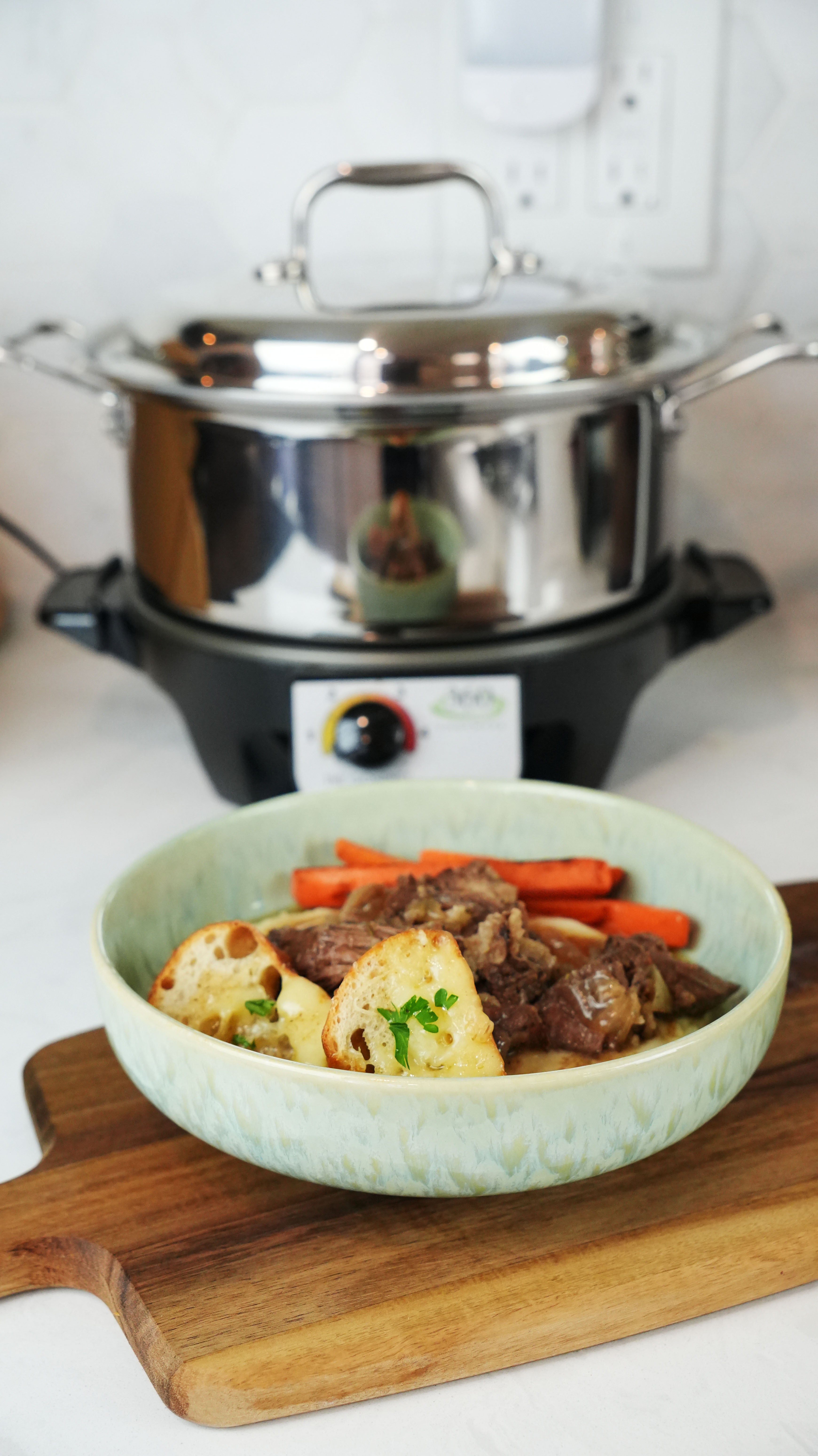 Pot roast with carrots and garlic toast served in front of a stainless steel slow cooker