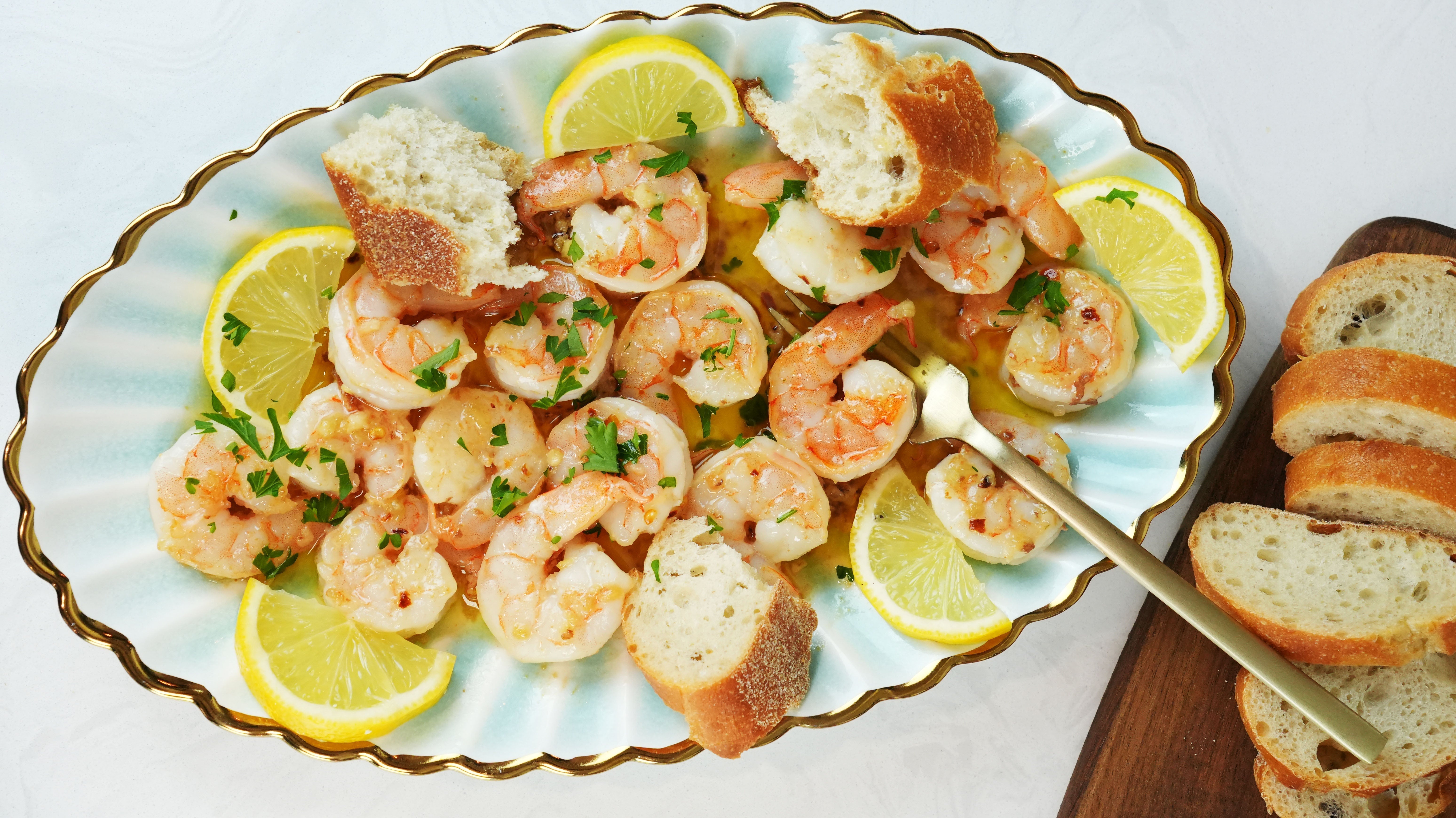 Shrimp scampi served on a scalloped platter with lemon wedges and crusty baguette slices