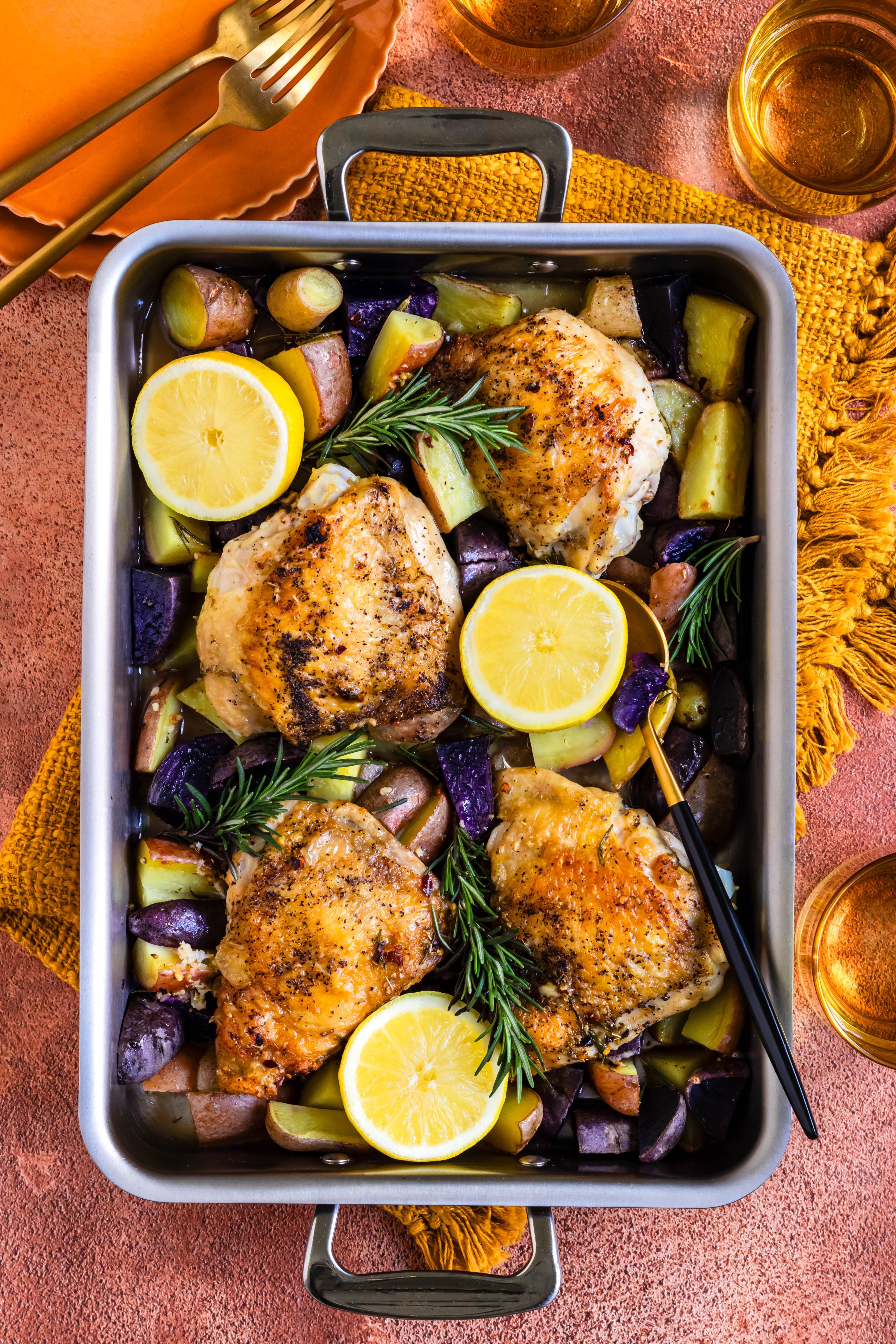 Roasted lemon rosemary chicken thighs with root vegetables in a stainless steel roasting pan