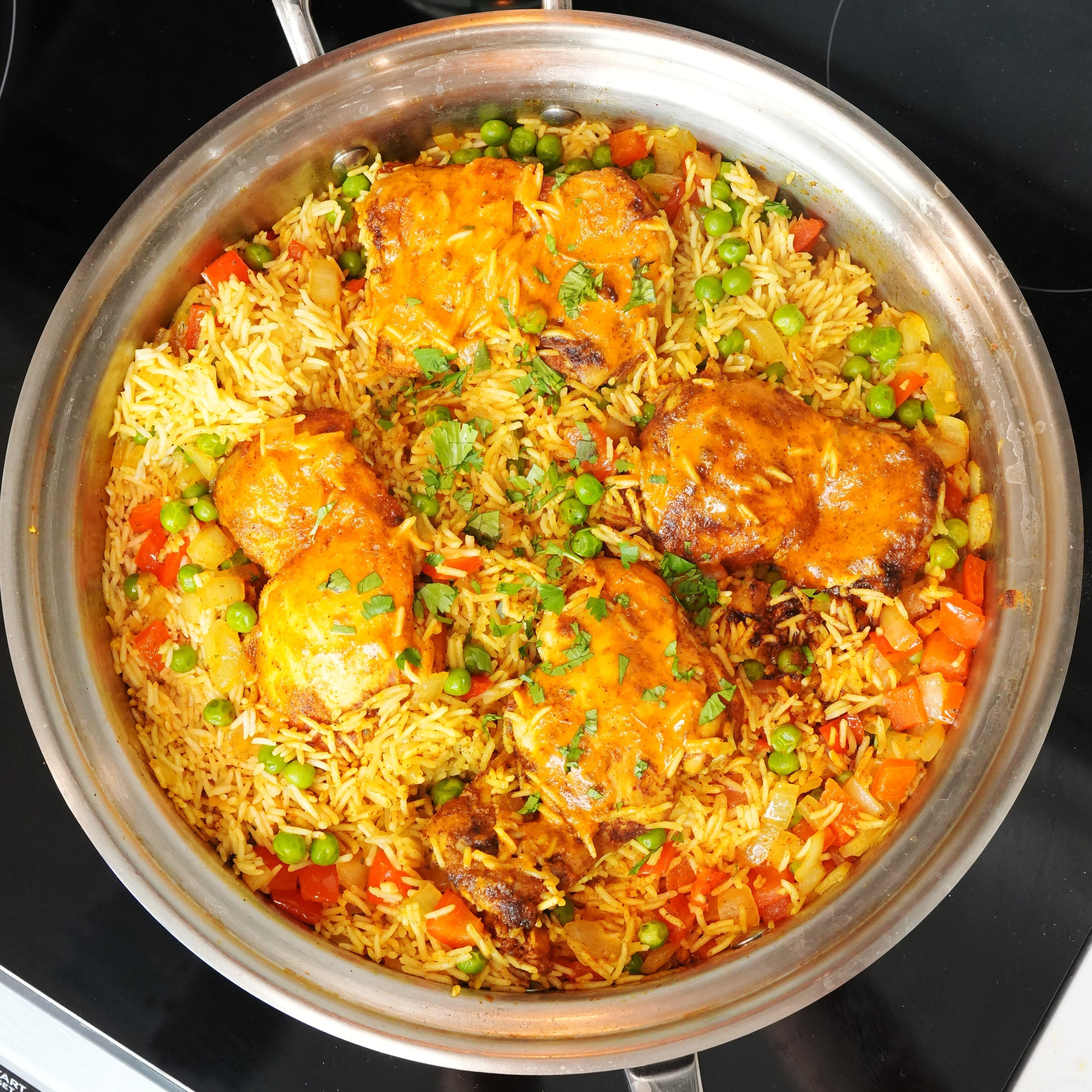 One-pan peri peri chicken thighs served on seasoned rice with peas and red bell pepper in a stainless-steel skillet