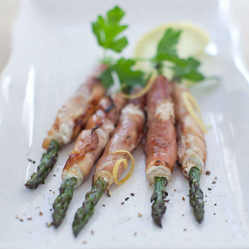 Five prosciutto-wrapped asparagus spears garnished with parsley and lemon slices