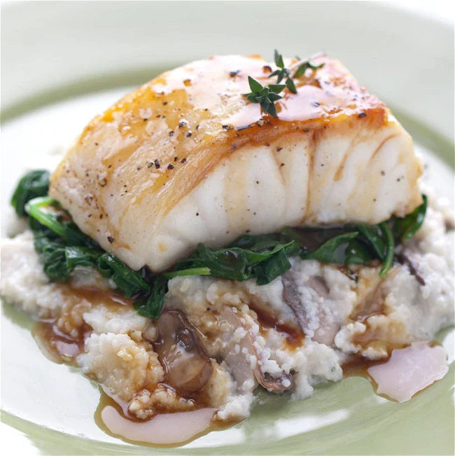 Pan-seared sea bass on a bed of wilted greens and creamy grits, garnished with thyme