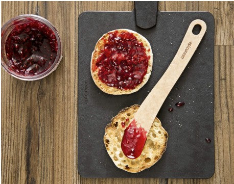 A cheese spreader with jam on a cutting board.
