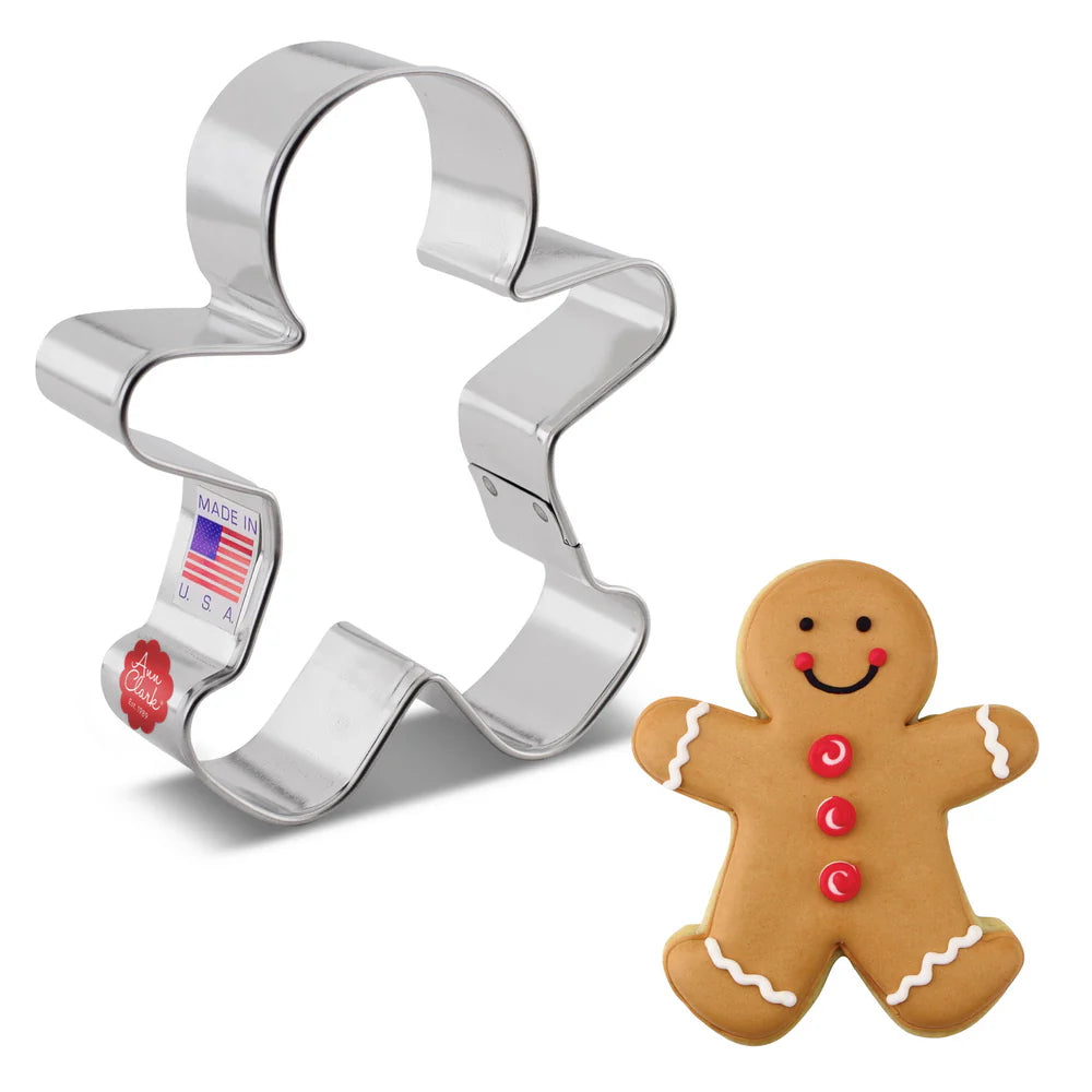 Gingerbread man cookie cutter next to a decorated gingerbread cookie with red buttons and icing.
