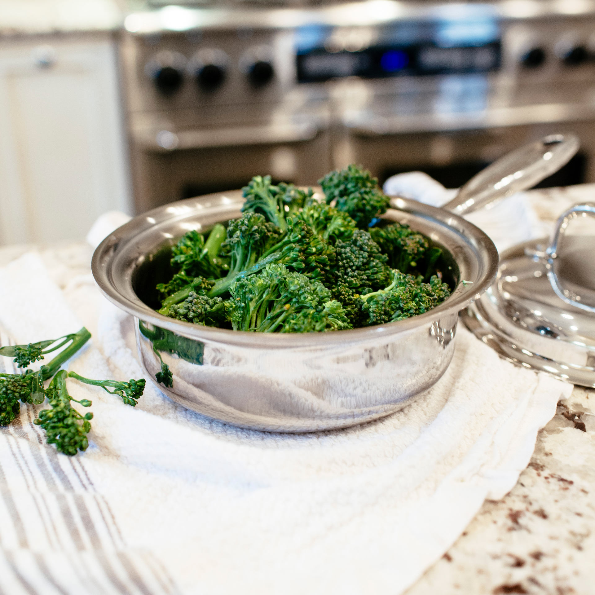 A stainless steel sauté pan filled with cooked broccoli on a kitchen countertop.