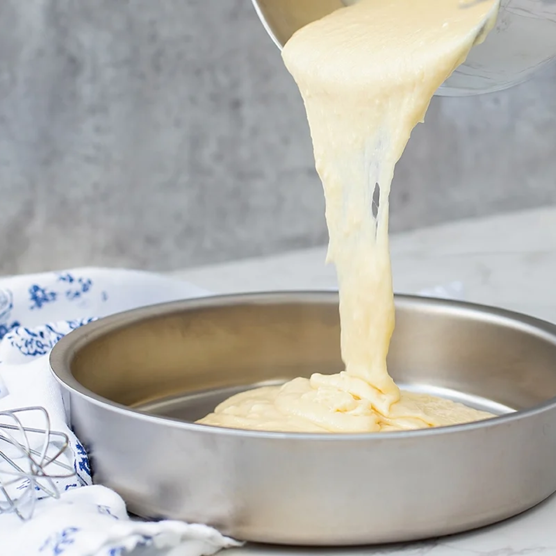 Pouring cake batter into a 9" round stainless steel cake pan