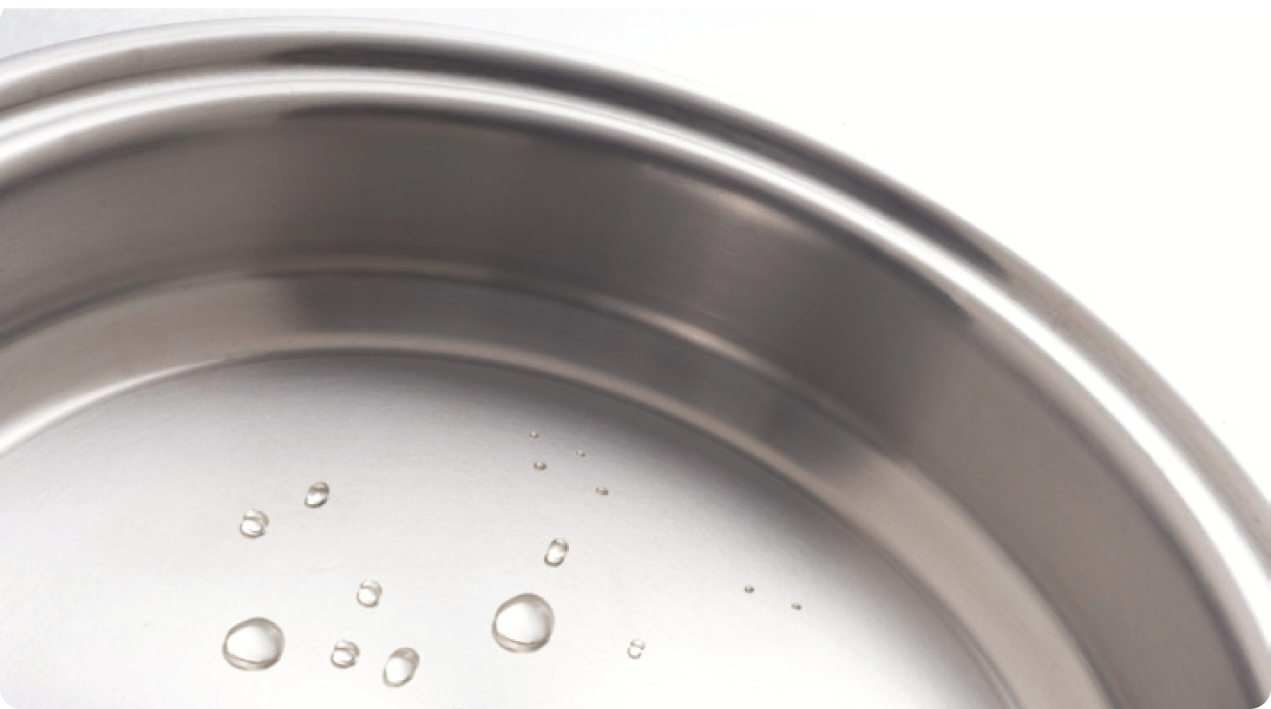 Close-up of water droplets on a stainless steel pan surface, indicating heat readiness for cooking.
