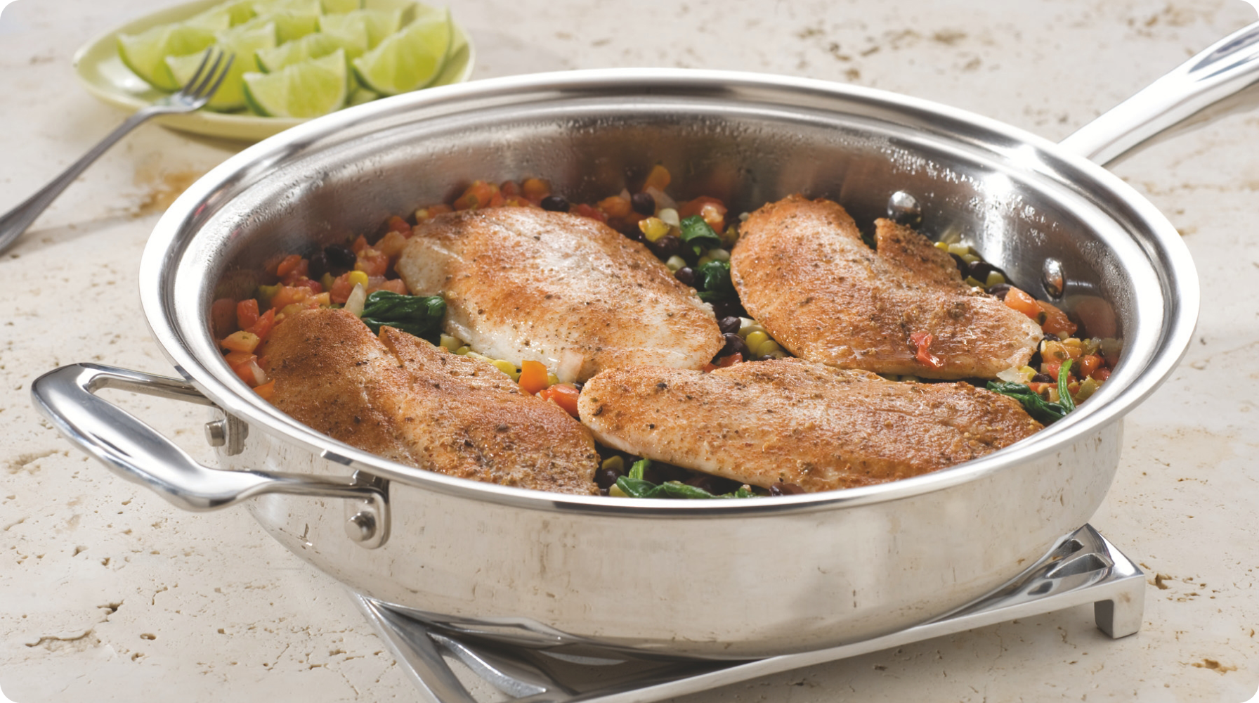 Cooked chicken fillets on a bed of vegetables in a stainless steel pan, with lime wedges in the background.