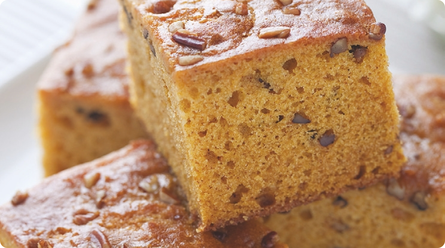 Close-up of a slice of pumpkin bread topped with nuts on a plate.