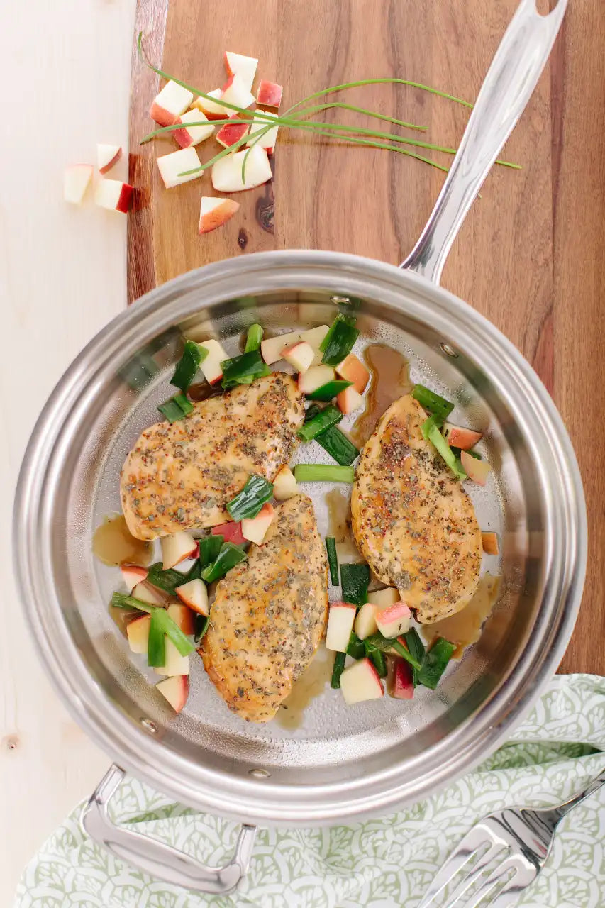 Stir-fried chicken with apples and green onions in a stainless steel pan on a wooden cutting board.