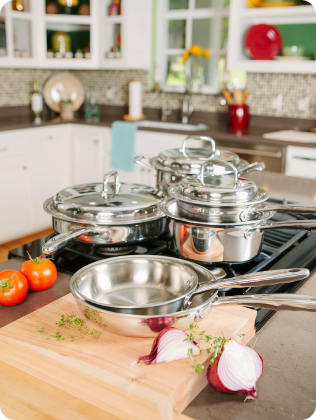 Stainless steel cookware on a stove with fresh tomatoes and onions on a cutting board.