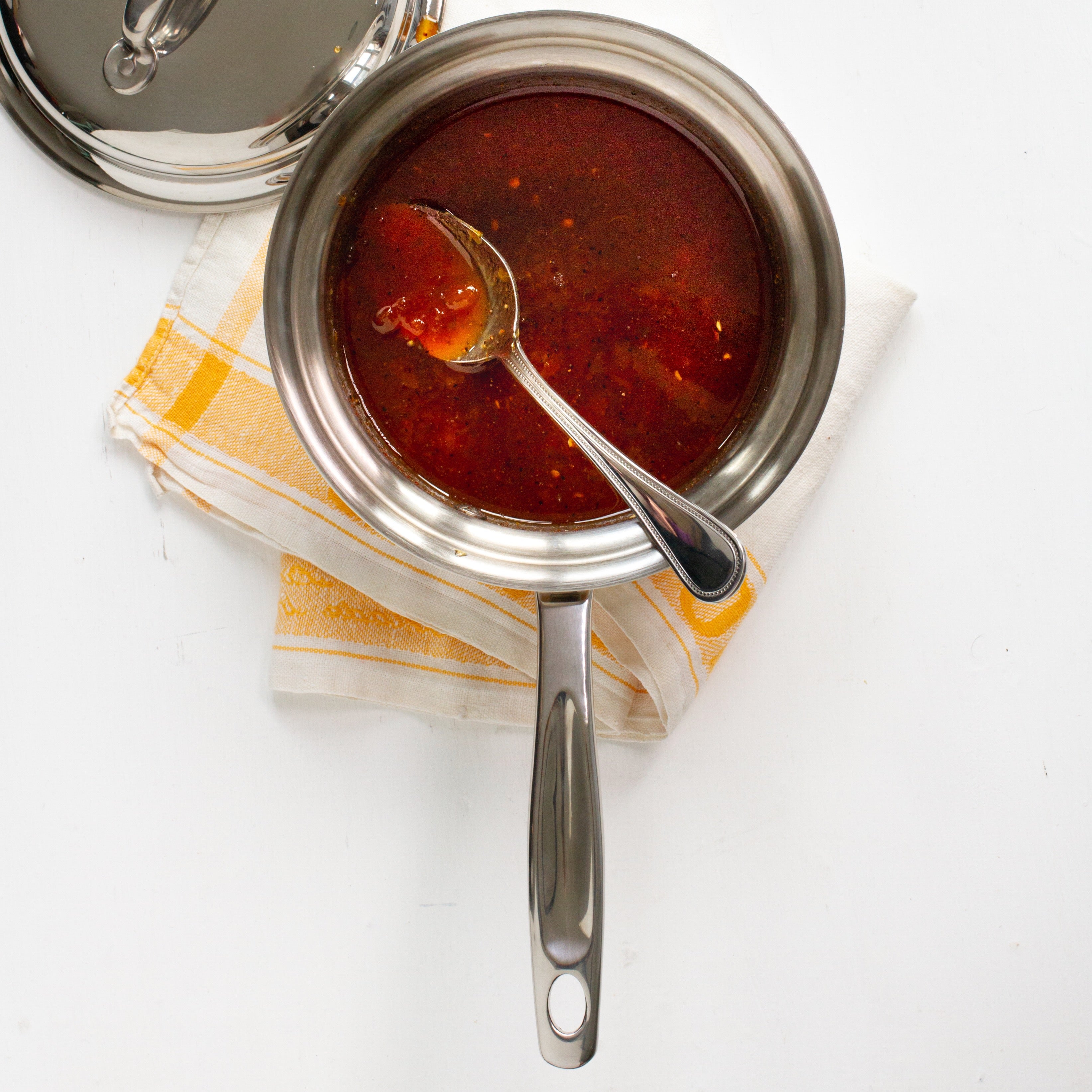 Stainless steel saucepan with sauce and spoon on a towel