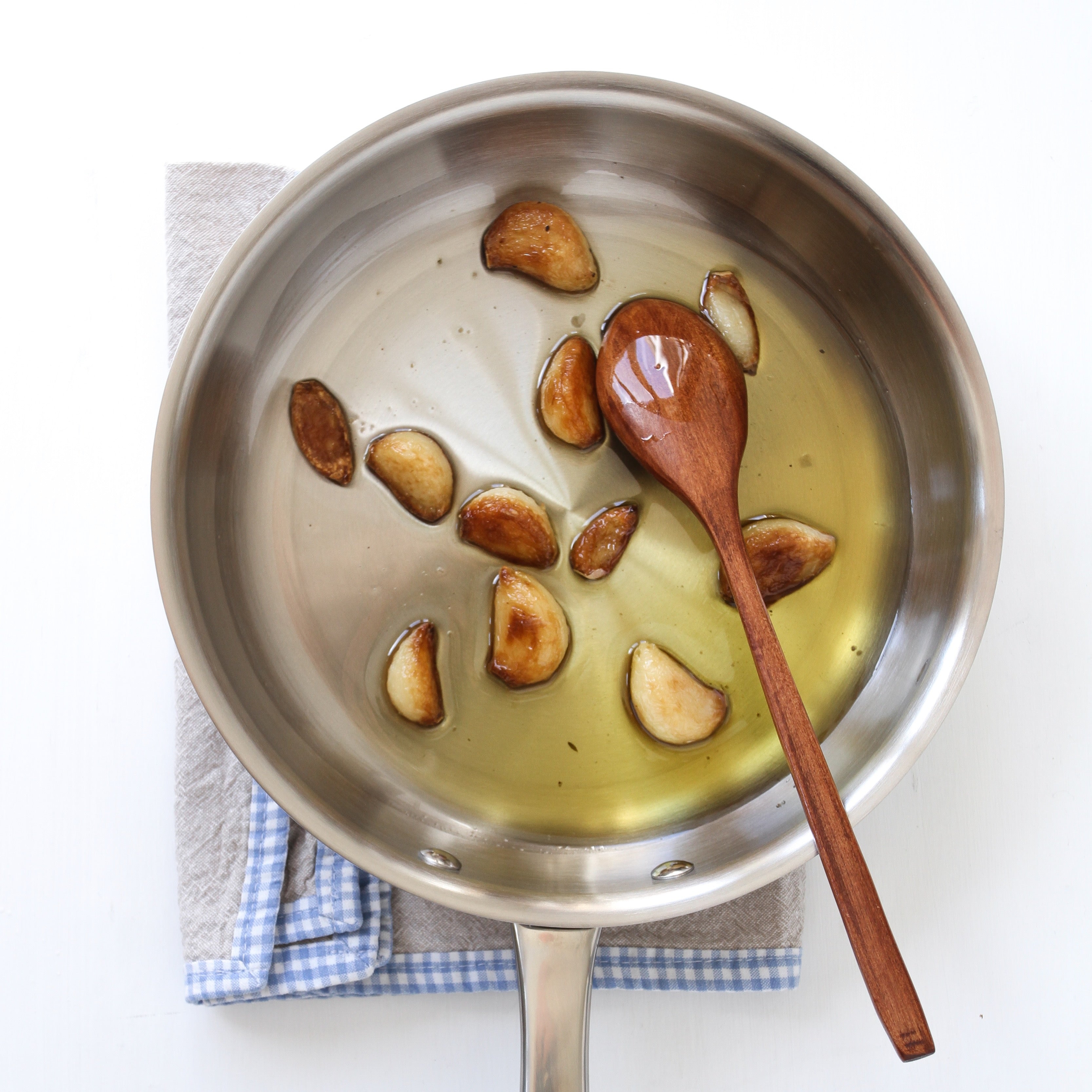 Stainless steel pan with garlic cloves in oil on a cloth