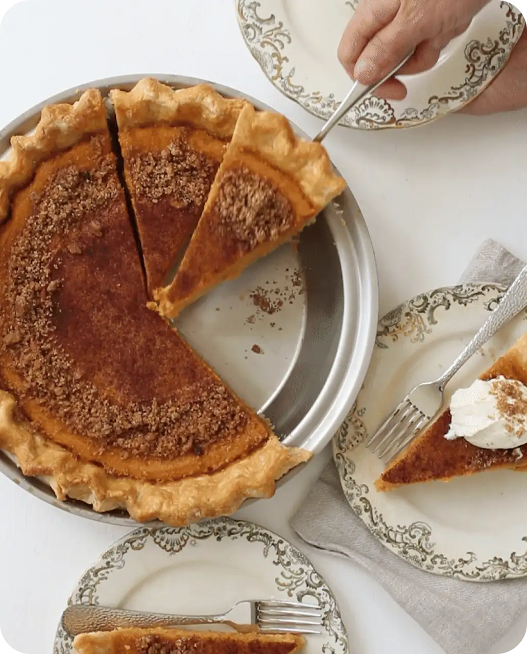 Pumpkin pie with a slice removed, served on a white tablecloth with decorative plates and forks.