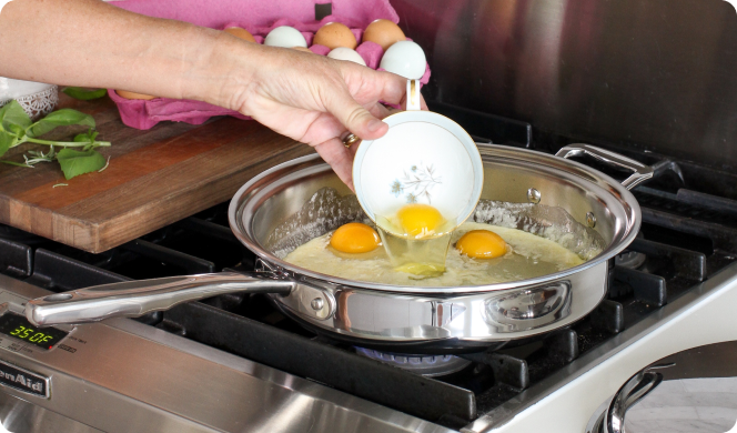 A hand pouring eggs into a stainless steel pan on a stove, illustrating cooking with quality cookware.