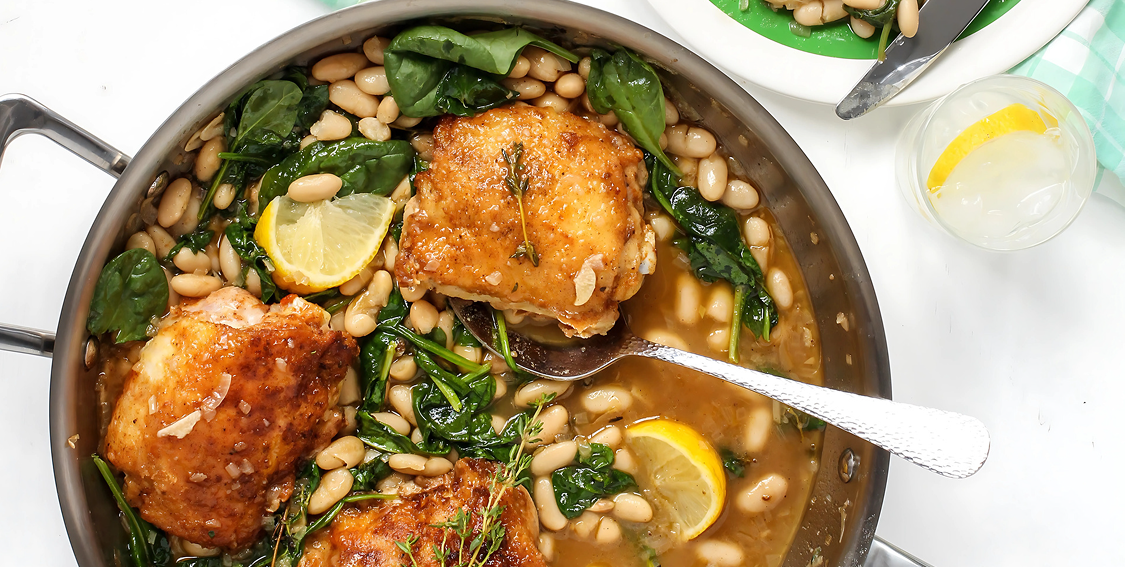 Skillet with chicken, beans, and spinach on a white background