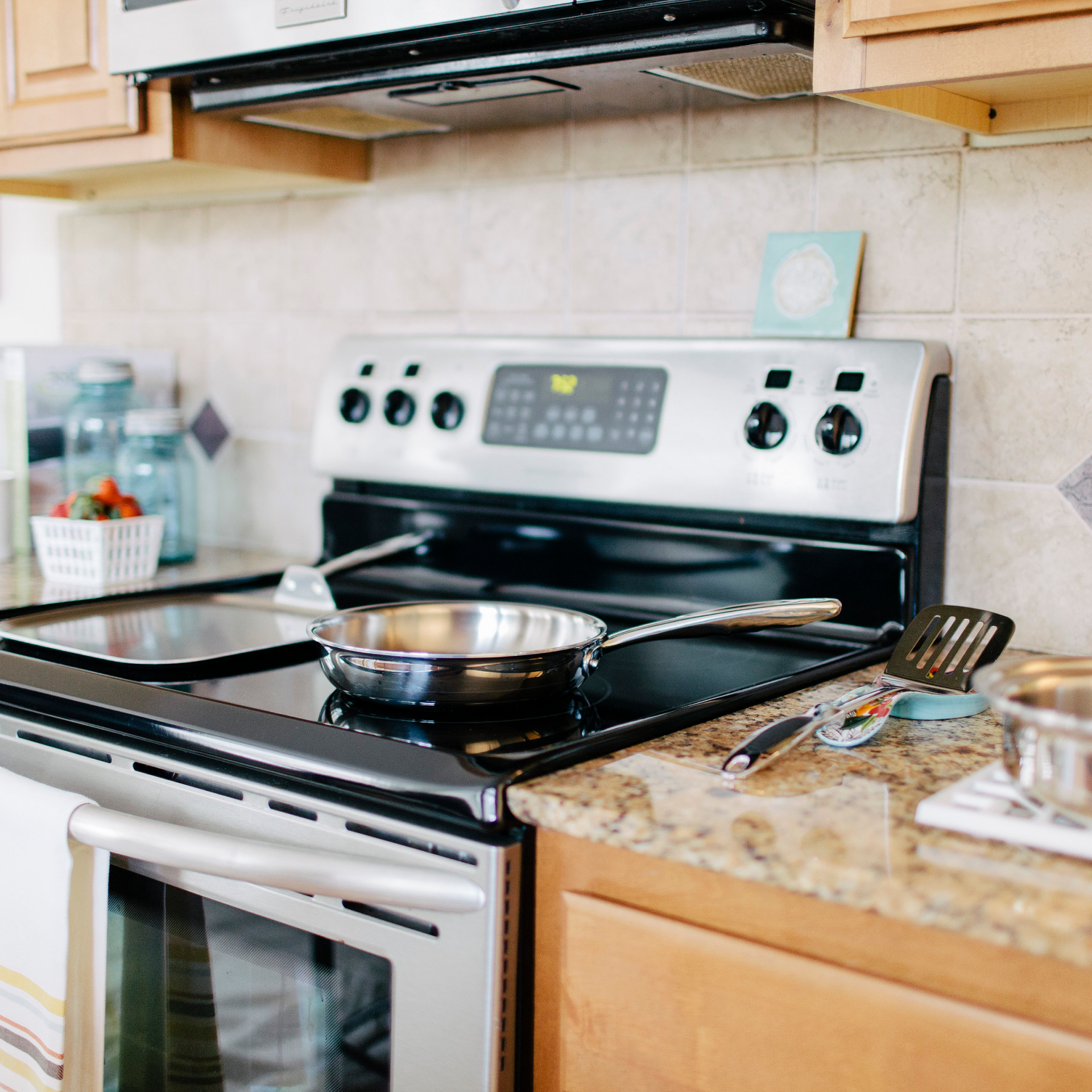 Stainless steel fry pan on a stove with utensils and ingredients nearby