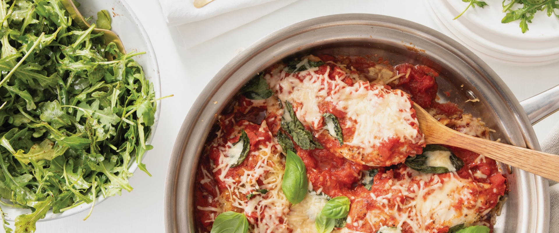Chicken Parmesan in a stainless steel pan with side salad on white table