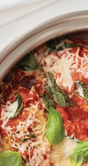 Close-up of a dish with tomato sauce, cheese, and basil leaves.