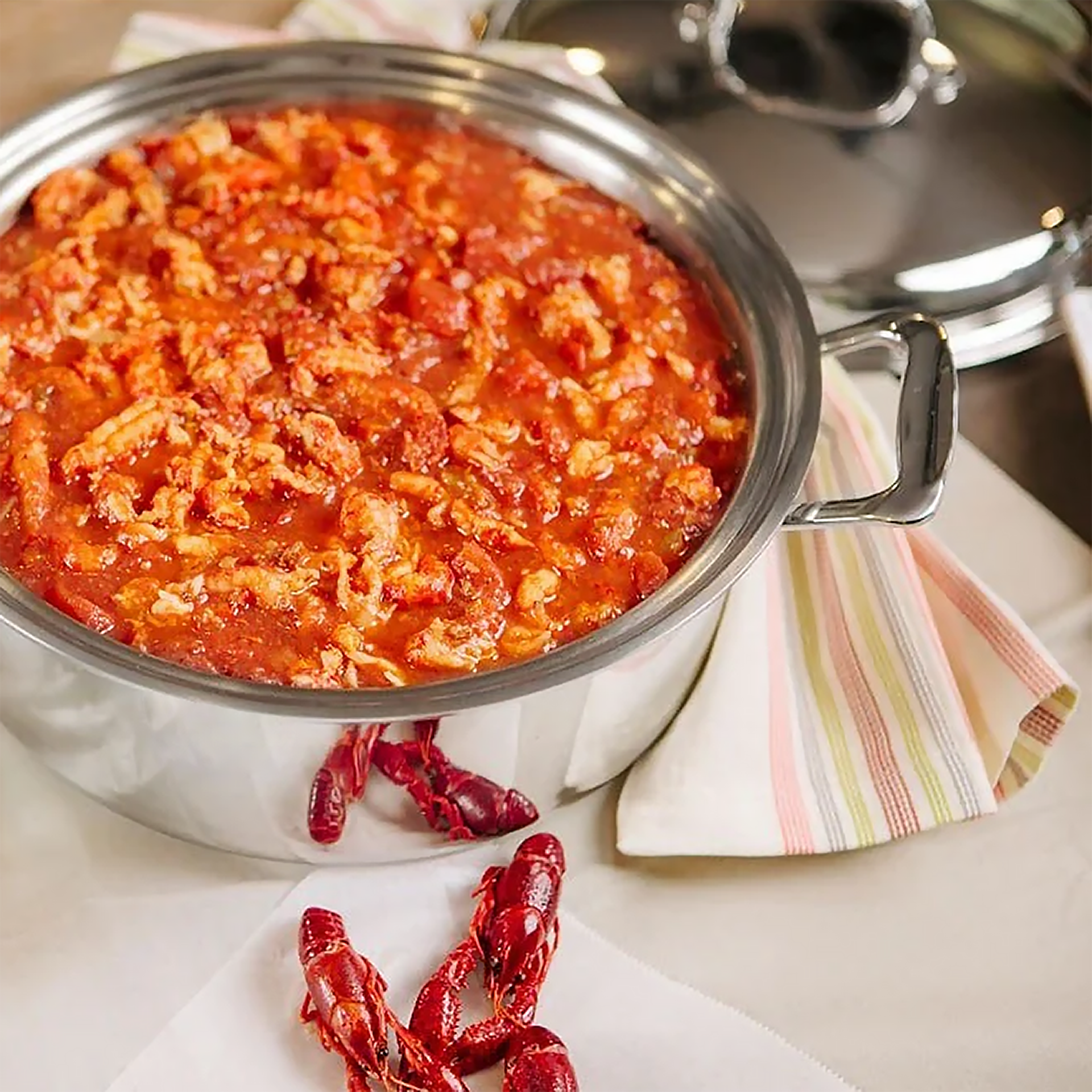 A 3 Quart saucepan filled with a seafood dish, placed on a table with a striped cloth.