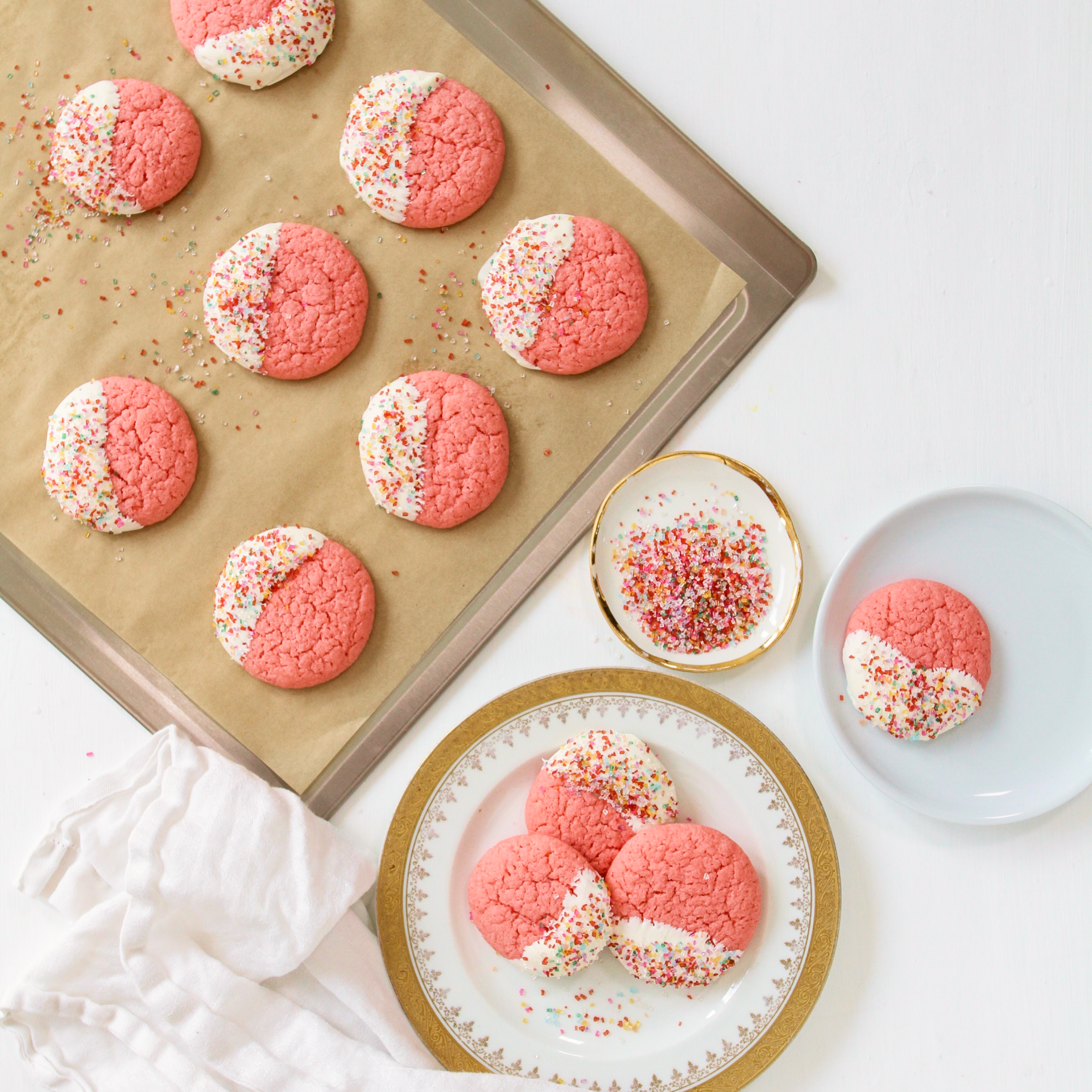 A tray of pink and white cookies with sprinkles, alongside plates of cookies and sprinkles.
