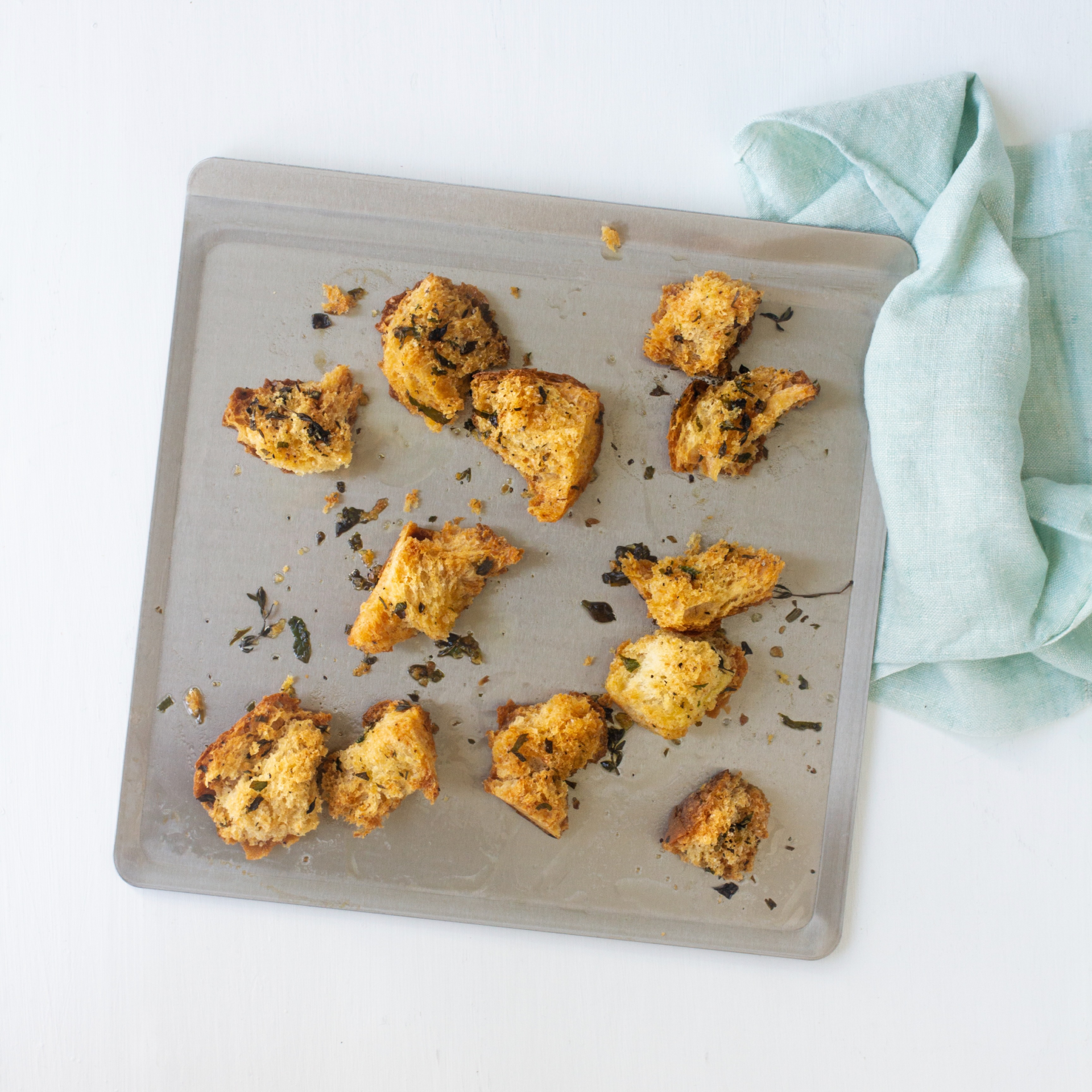 Baked pieces of bread on a stainless steel cookie sheet with a light blue cloth nearby.