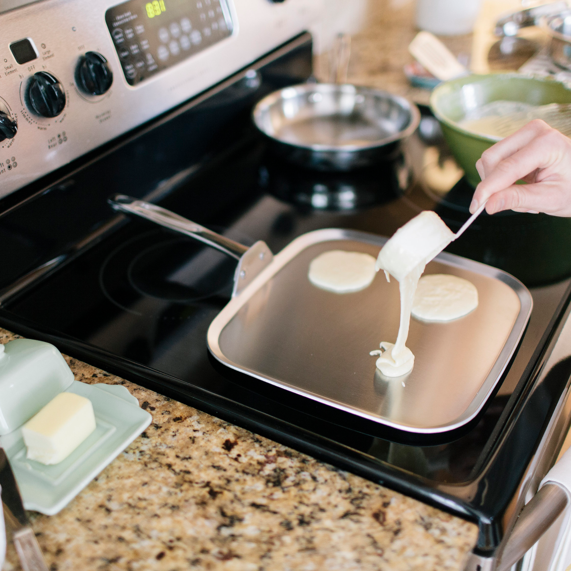 A hand pouring batter onto a griddle on a stove.