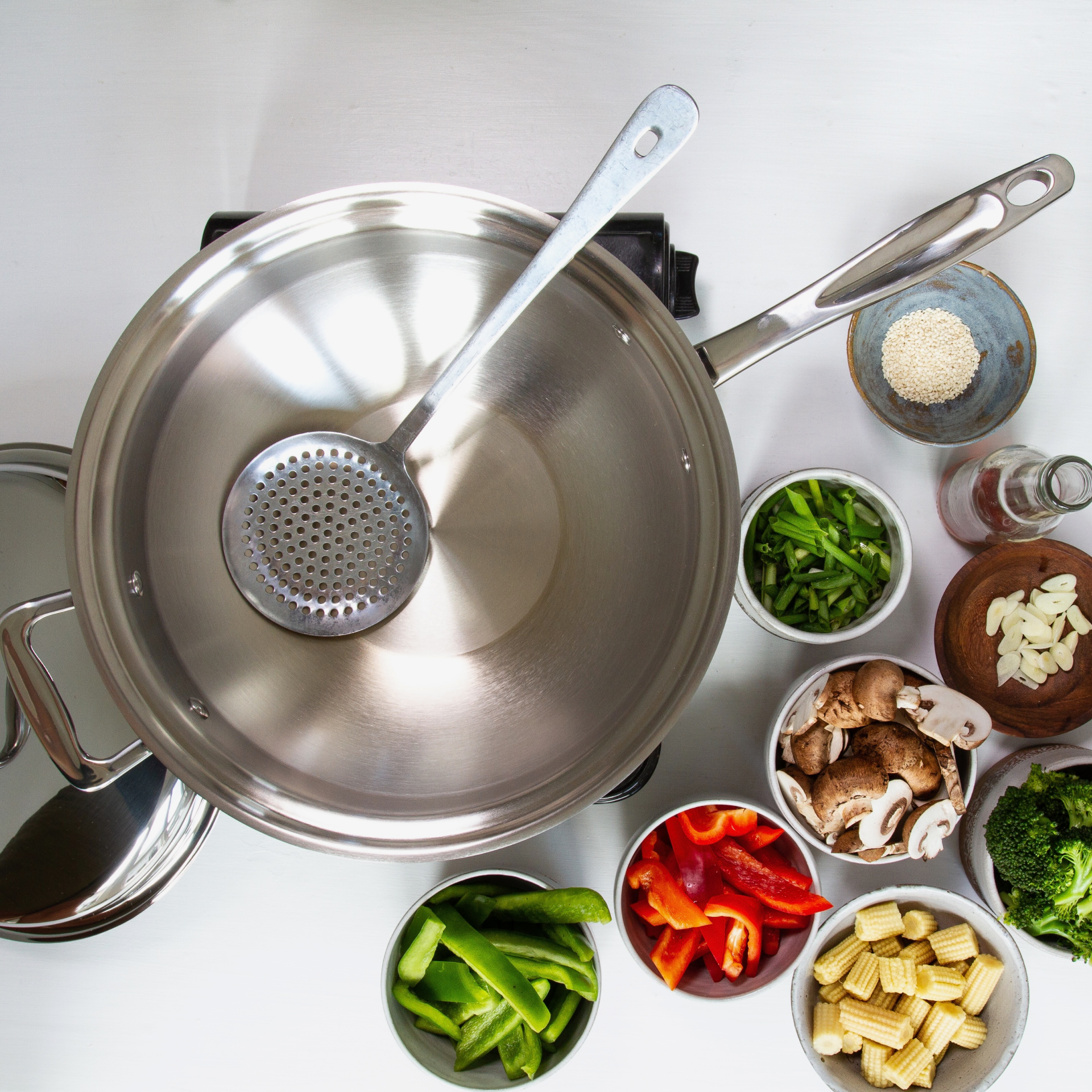 Stainless steel wok with vegetables and cooking utensils arranged around it