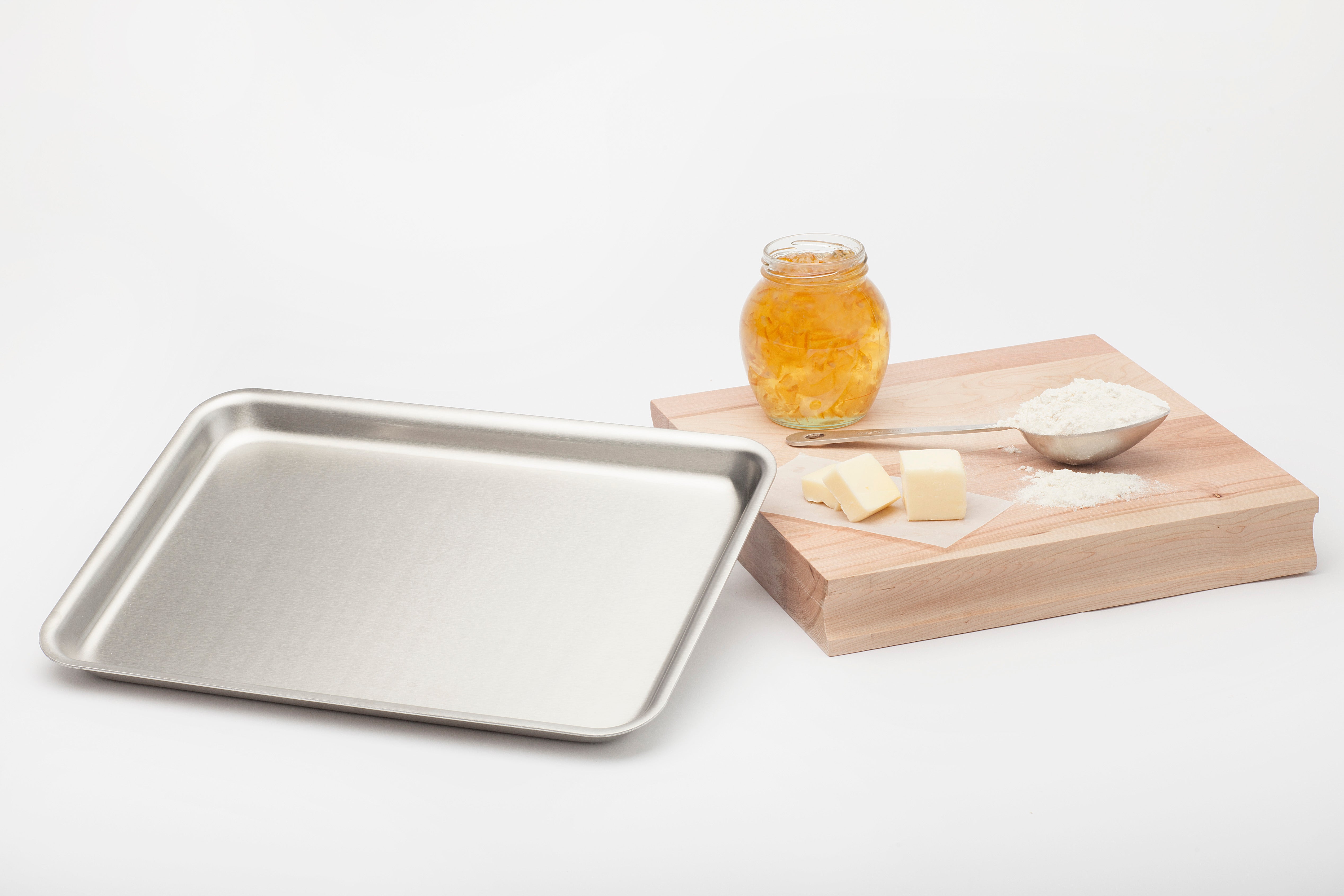 Stainless steel jelly roll pan with butter, flour, and a jar of jelly on a wooden board