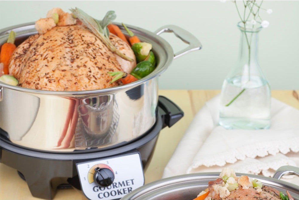 A 4-quart slow cooker with a chicken and vegetables inside, placed on a base, alongside another dish of food.