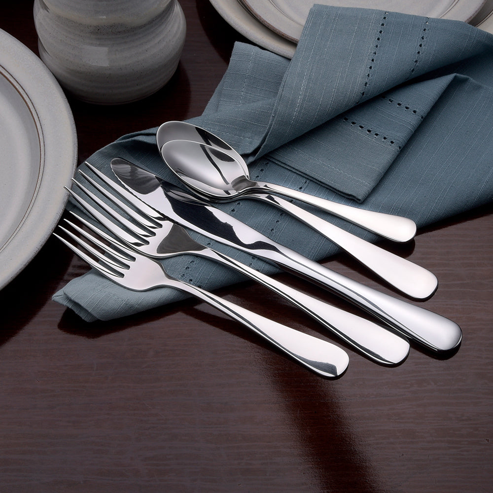 Annapolis 45 Piece Set flatware displayed on a blue napkin with plates in the background