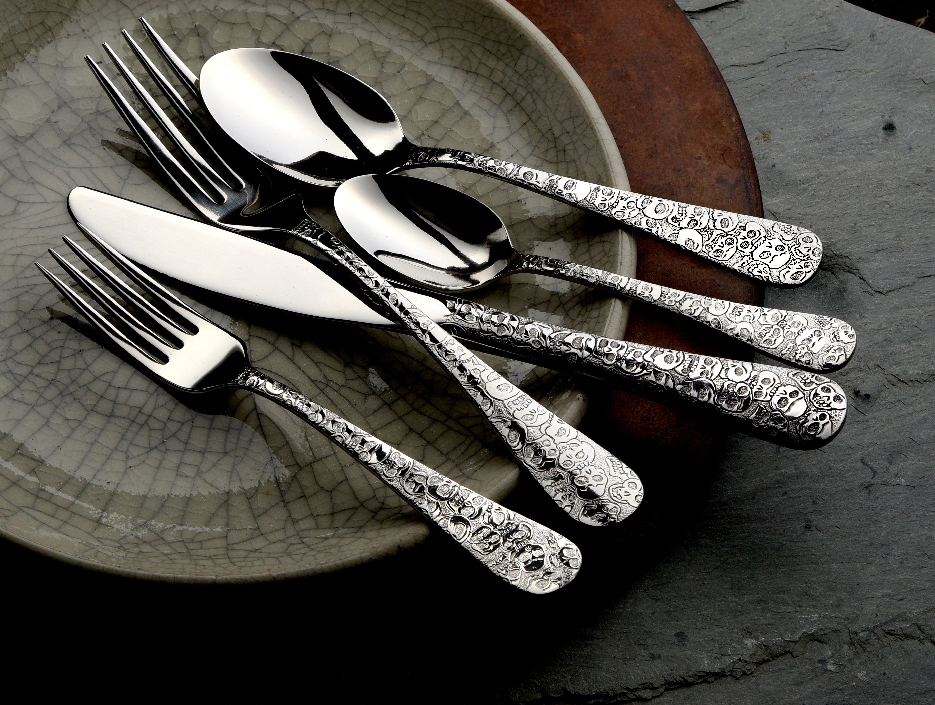 Calavera (Skull) flatware set featuring intricate skull designs on handles, displayed on a plate.