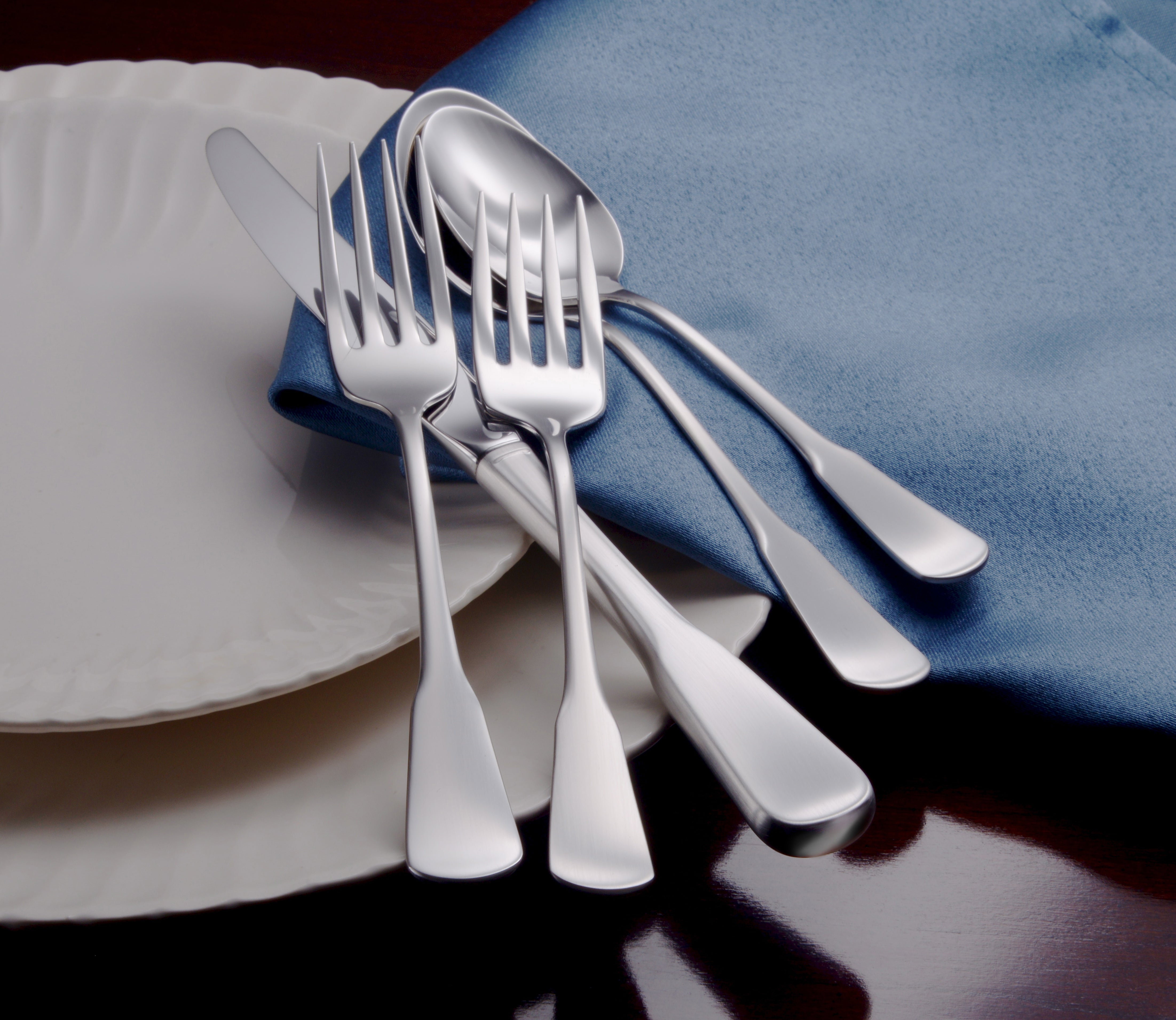 Candra 65 Piece Set flatware displayed on a blue napkin and plate