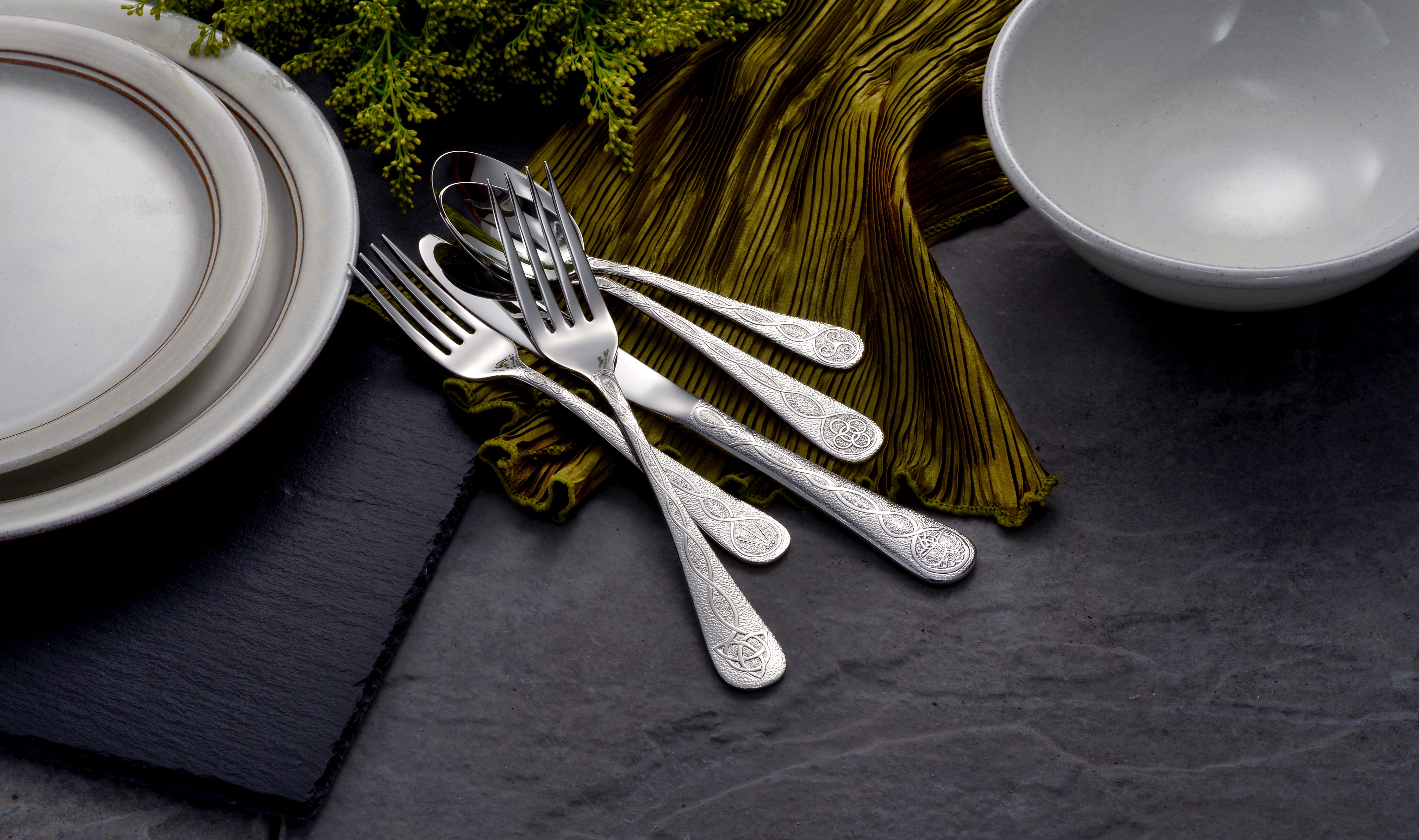 A set of silver cutlery and dishware on a dark surface with a green cloth.