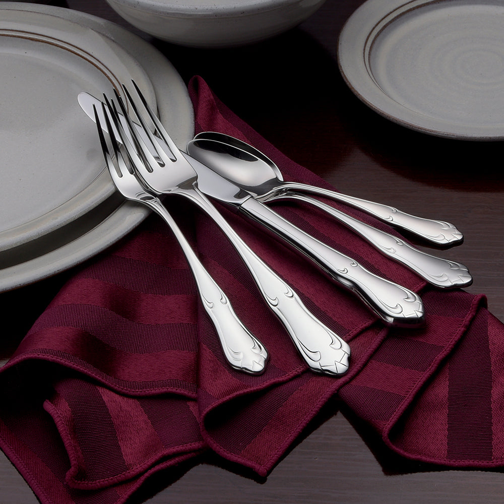 Champlin 65 Piece Set flatware displayed on a table with plates and a maroon napkin