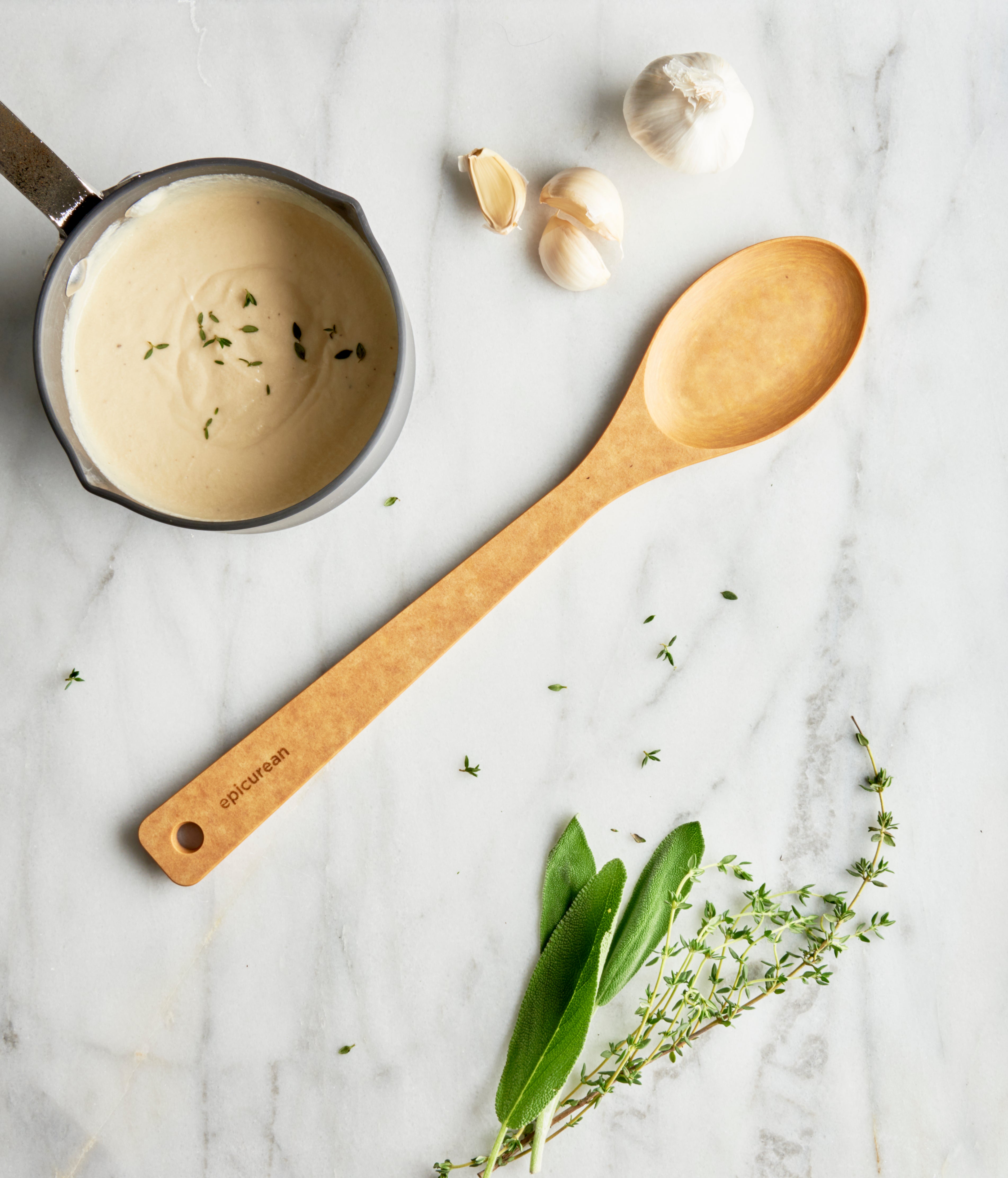 Natural large spoon spatula on a marble surface with herbs and garlic, showing its design and usage context.