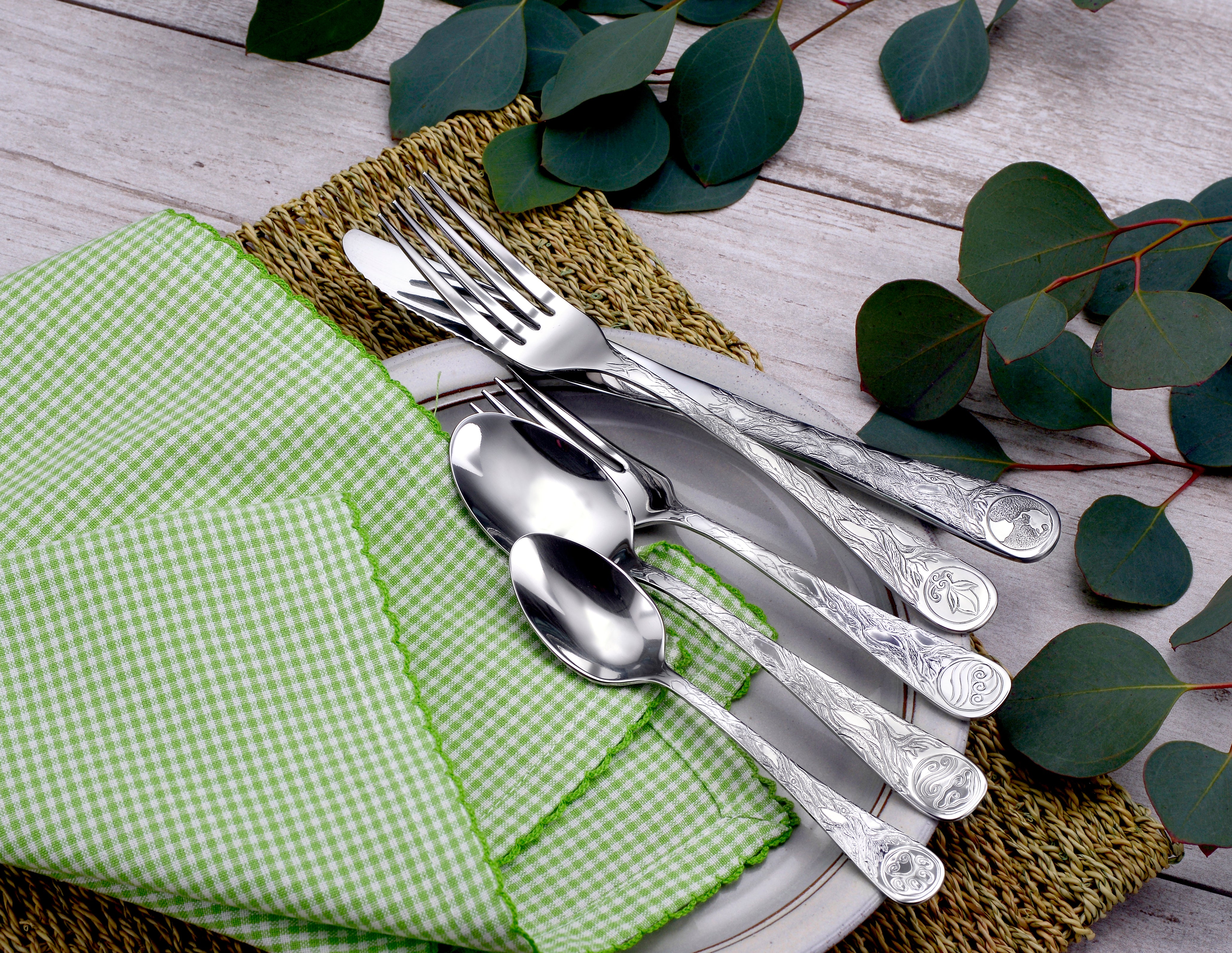 Earth Pattern Flatware set displayed on a plate with a green checkered napkin and eucalyptus leaves
