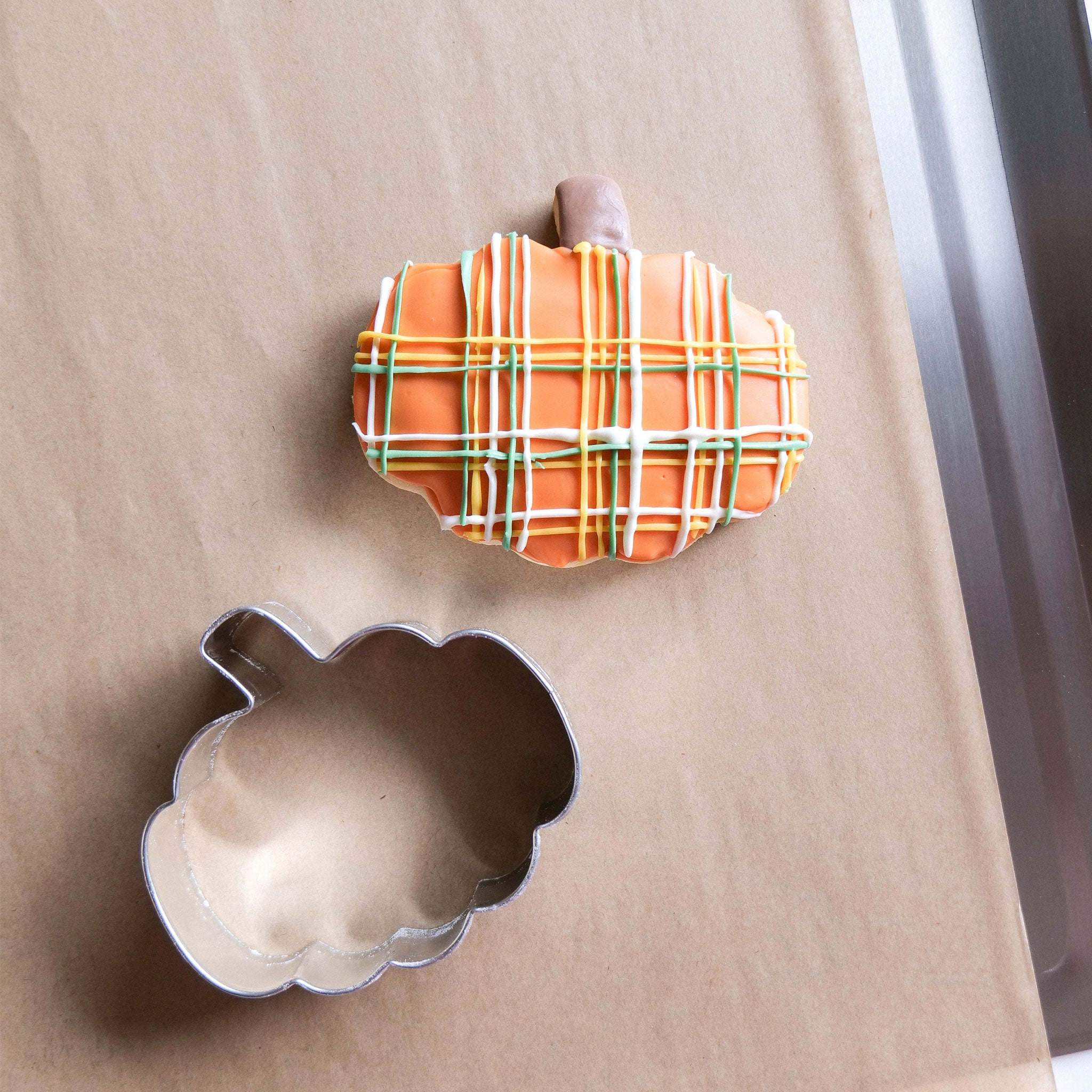 A 3-inch pumpkin-shaped cookie cutter next to a decorated pumpkin cookie.